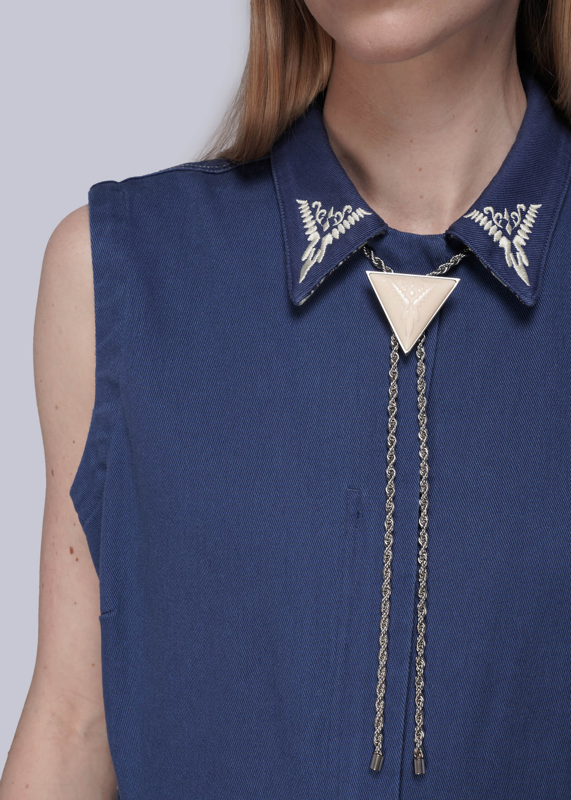 Navy blue sleeveless top with embroidered collar and silver bolo tie on a plain background