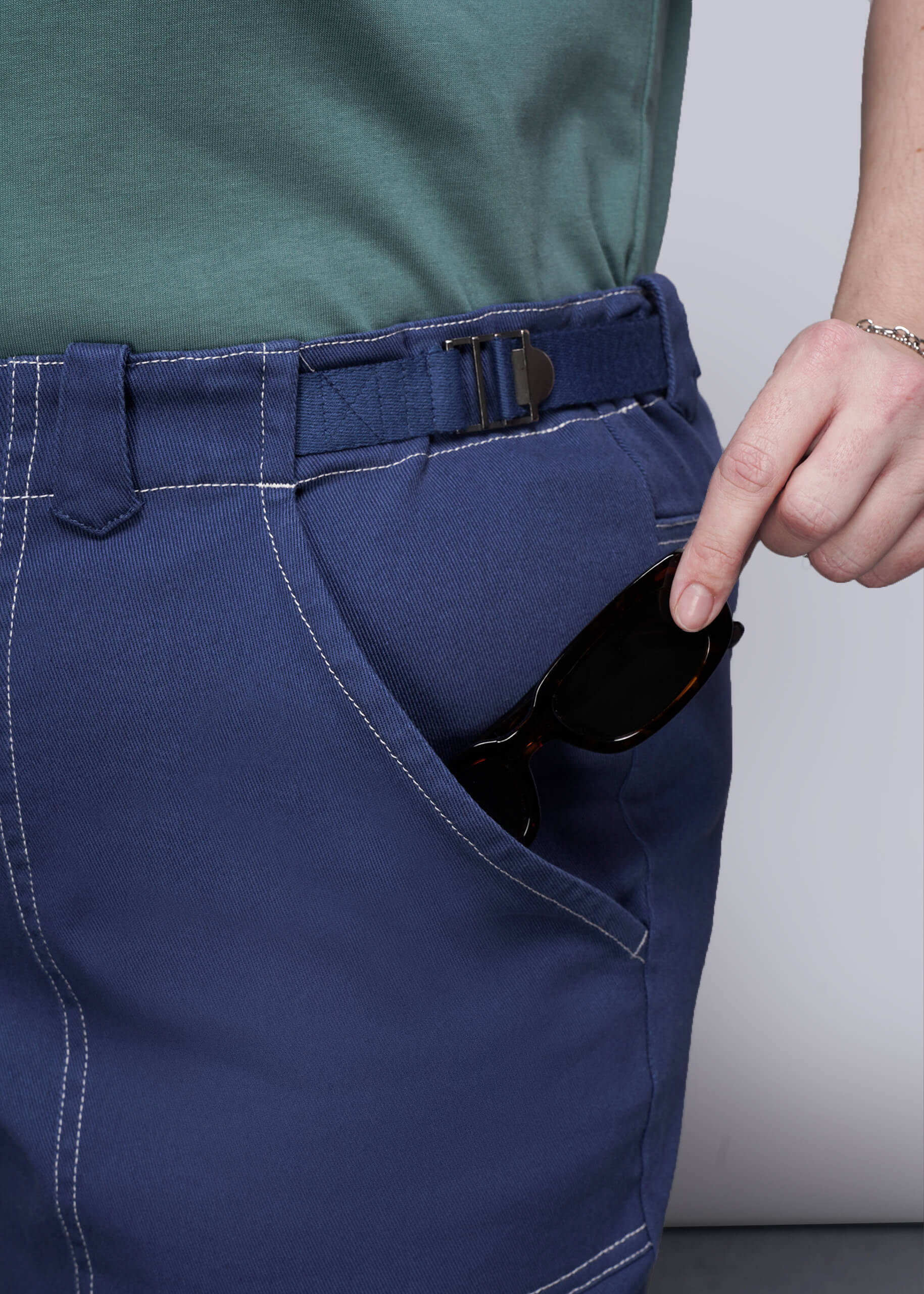 1X=Person wearing blue denim pants, placing sunglasses inside front pocket.