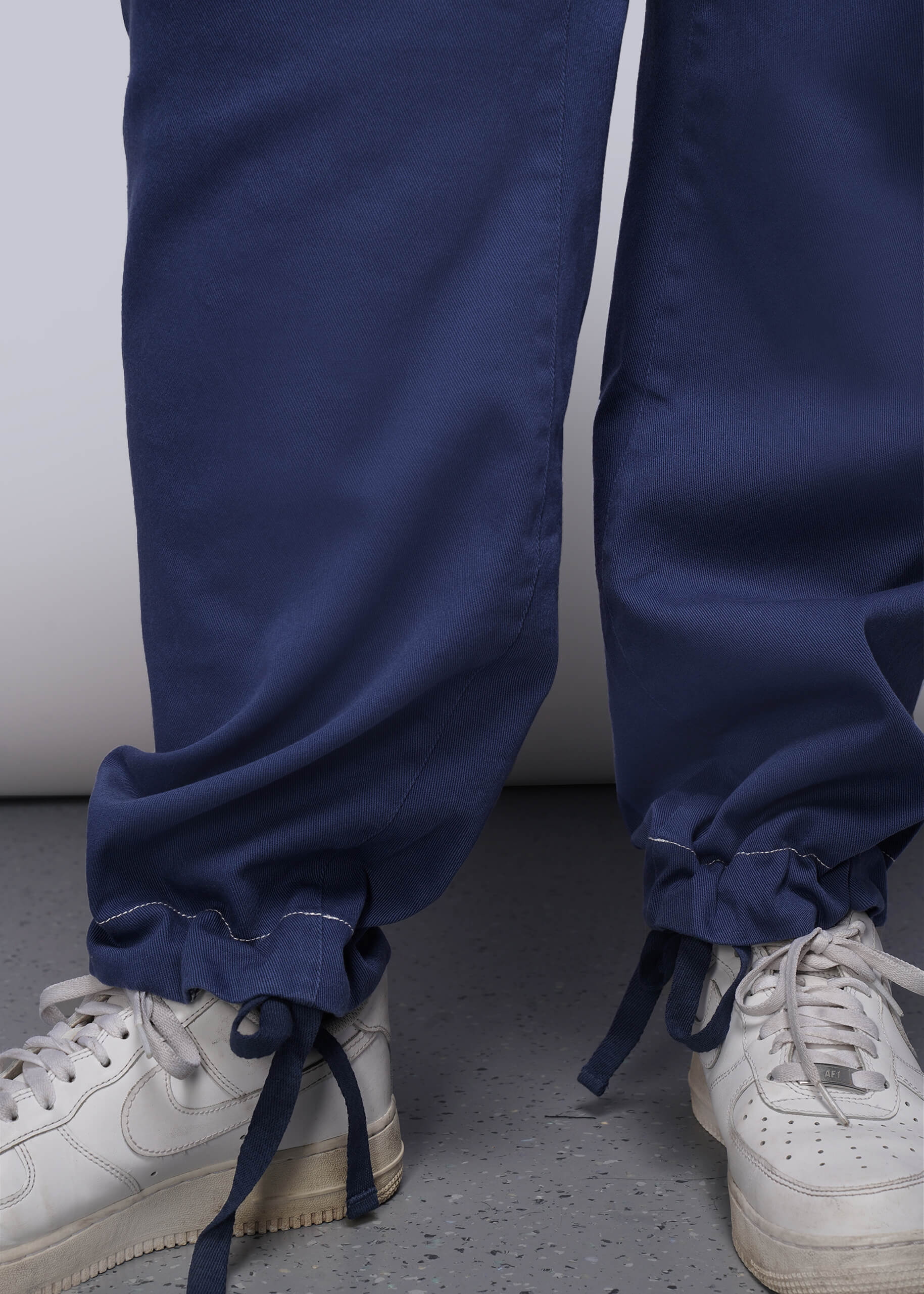 1X=Navy blue denim pants with drawstrings by ankle, worn over white sneakers on a neutral background