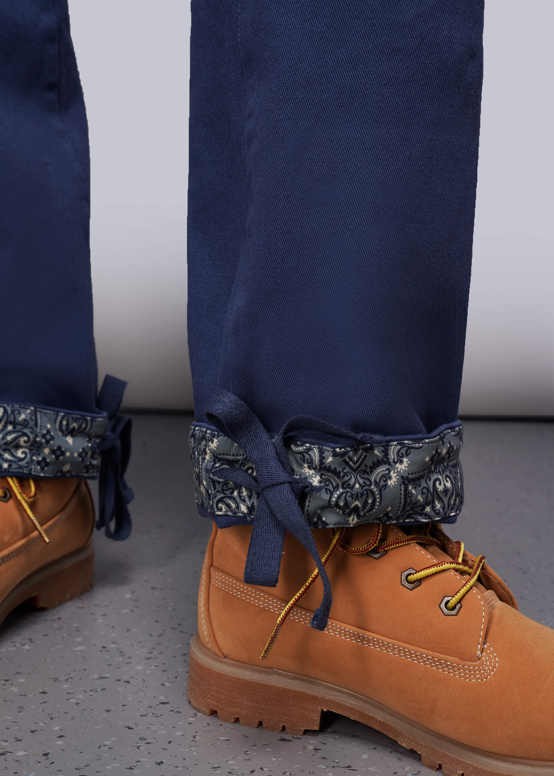 S=Close up of blue denim pants with patterned cuffs and tan boots on a gray floor.