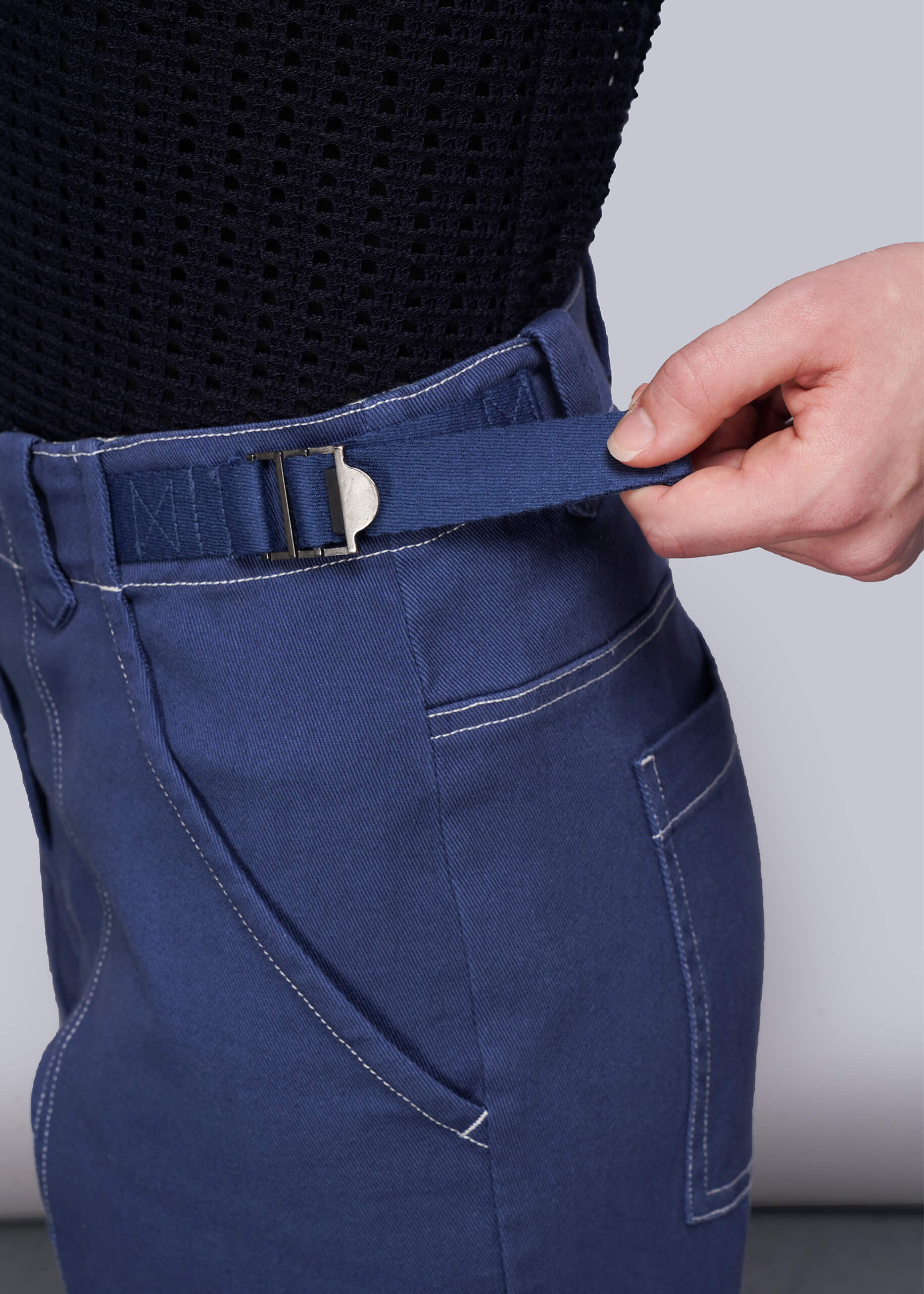 S=Person adjusting the adjustable waist on blue denim pants against a neutral background