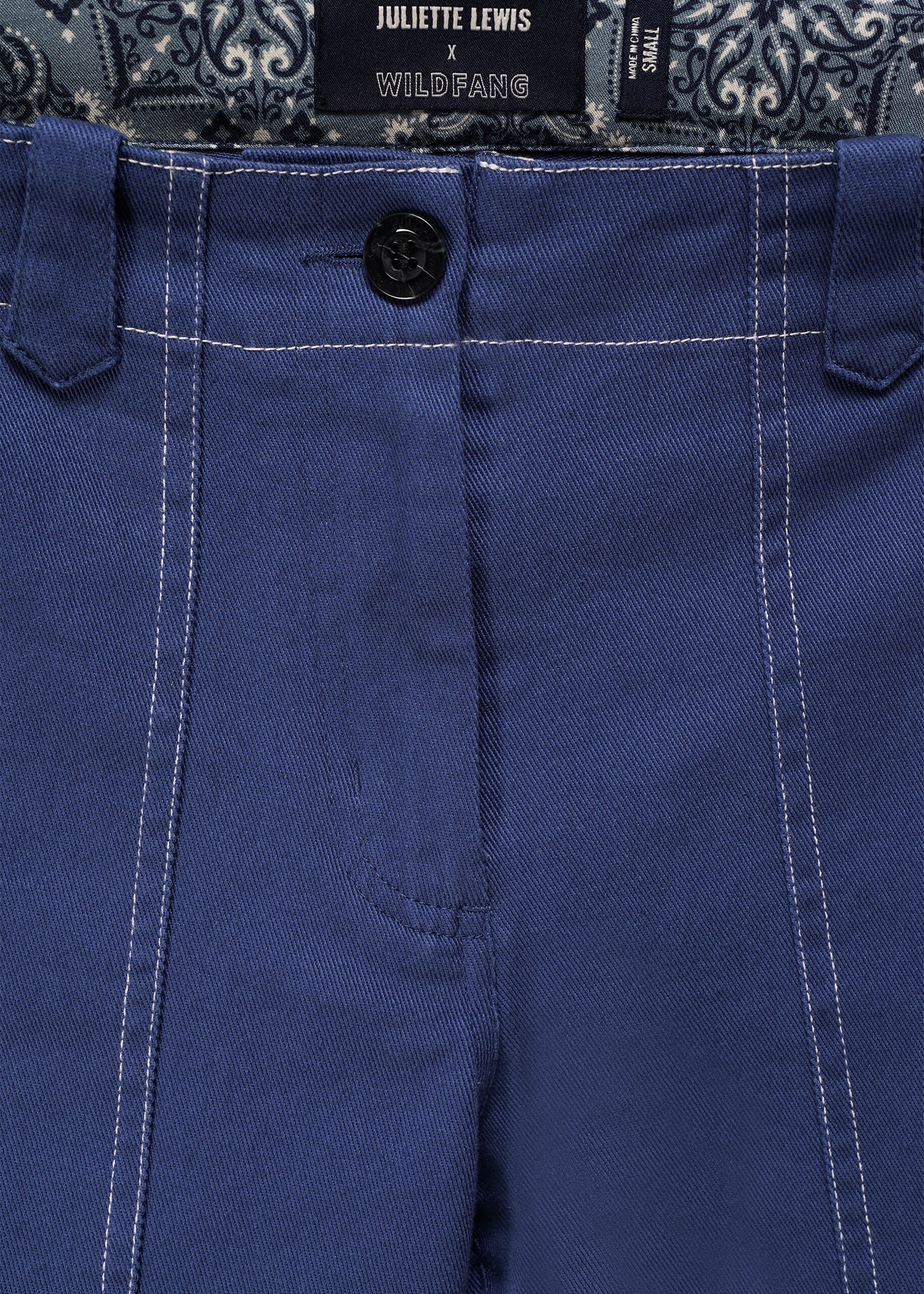 S=Close-up of blue denim pants with a patterned fabric waistband and Juliette Lewis x Wildfang brand label.