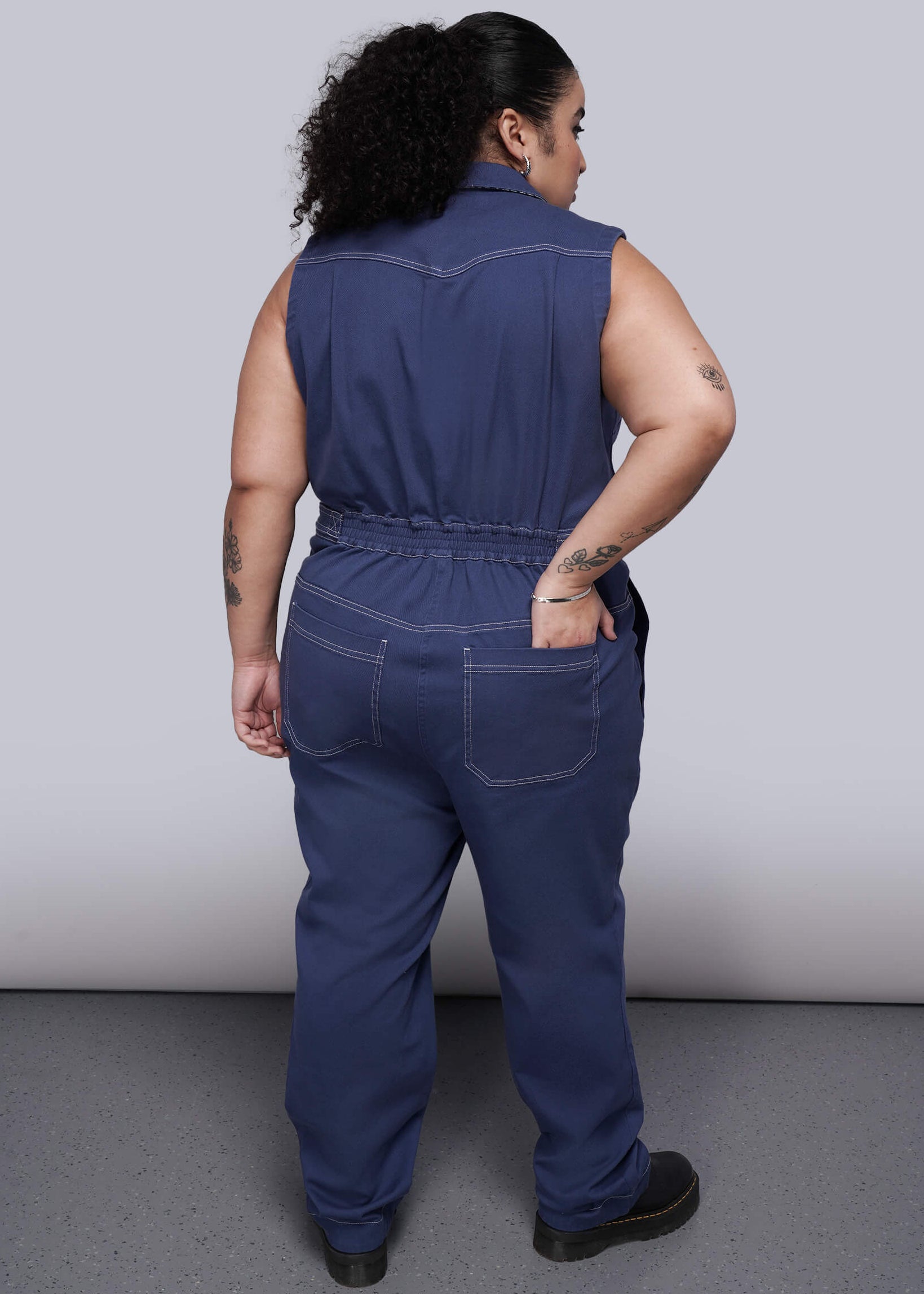 1X= Back of person wearing a blue jumpsuit against a plain background