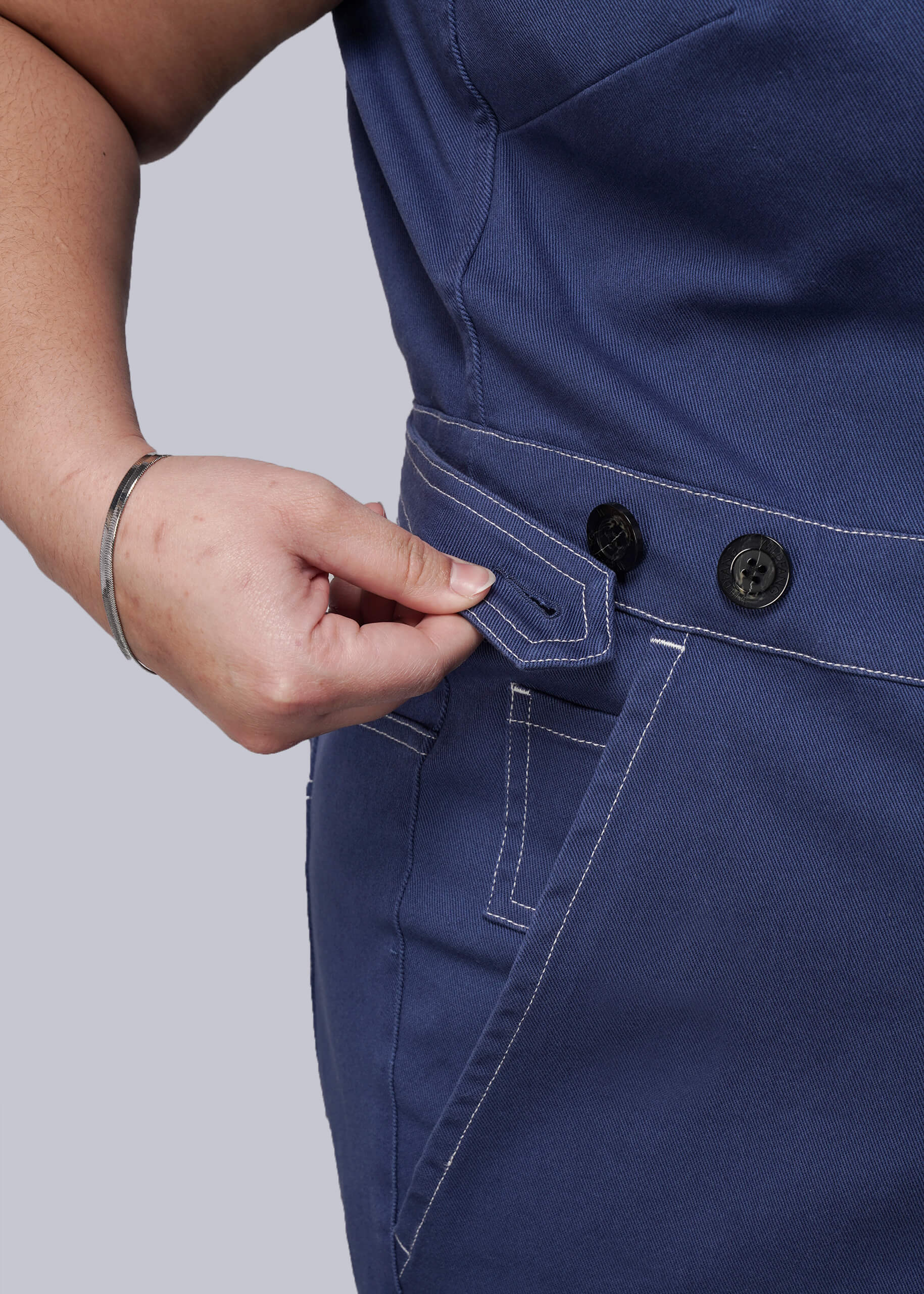 1X=Person wearing blue denim coverall with a close-up of the waistband on a light gray background
