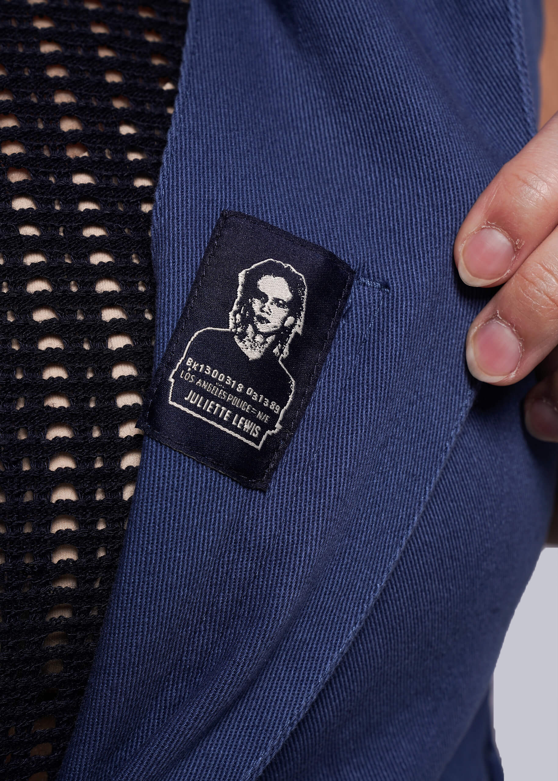 1X=Close-up of a blue denim coverall with an interior label featuring an image of Juliette Lewis.