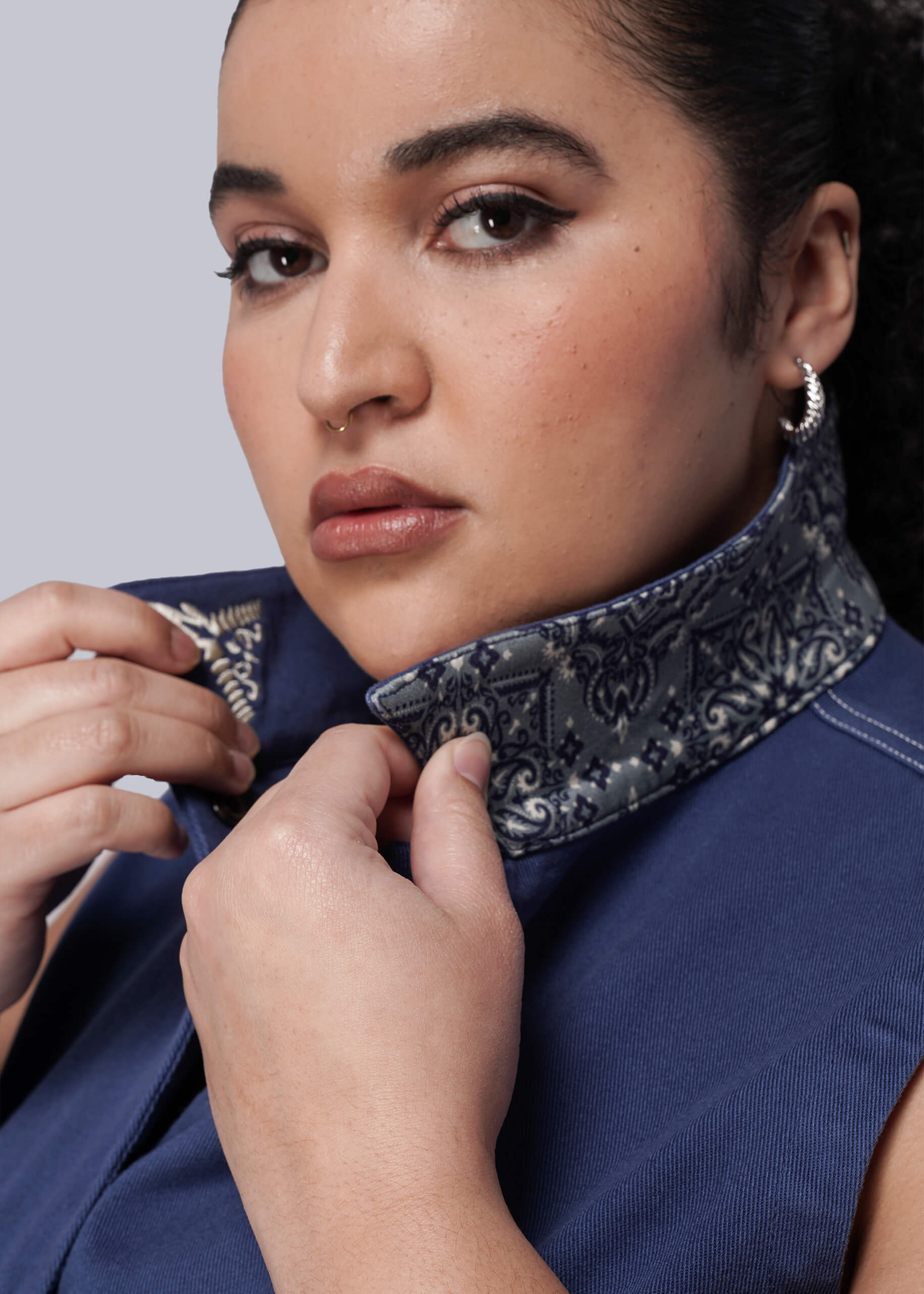 1X=Woman adjusting a decorative collar on a blue denim jumpsuit against a plain background