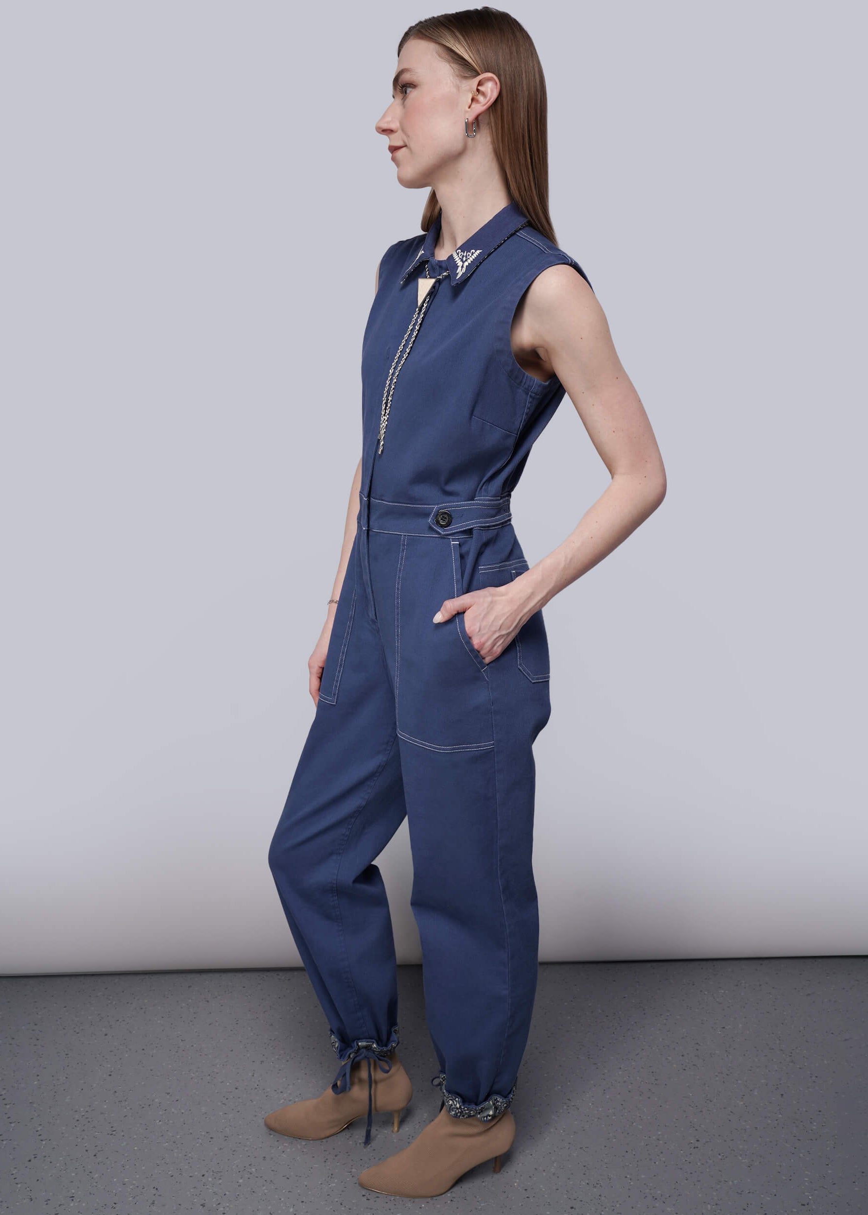 S=Woman wearing a blue sleeveless denim jumpsuit against a plain background