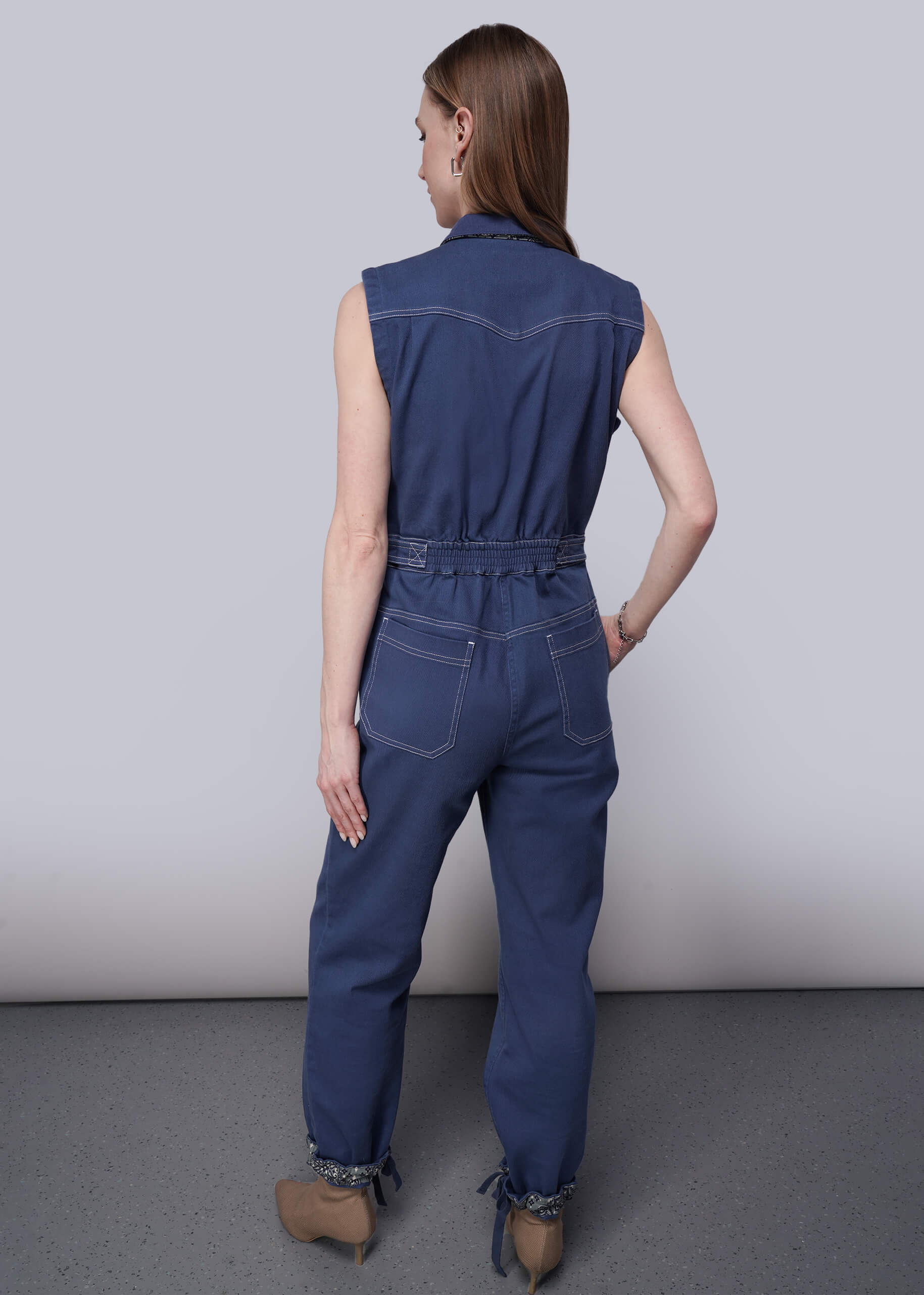 S=Woman wearing a sleeveless blue denim jumpsuit against a plain background