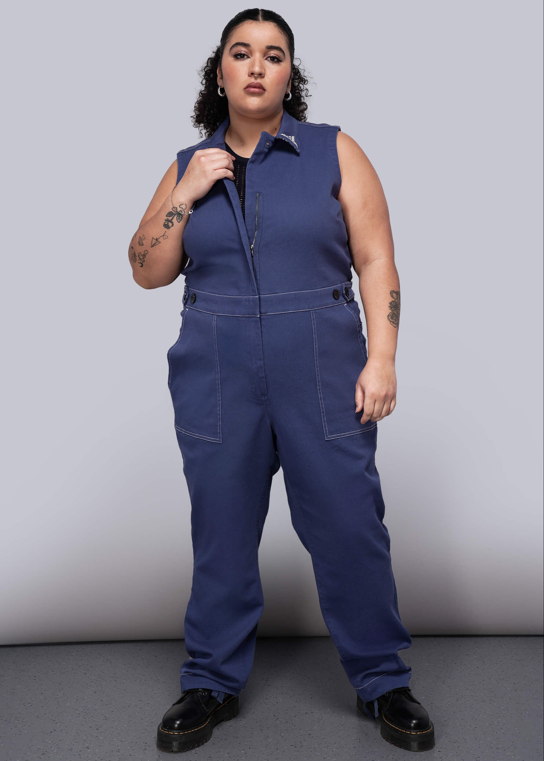 1X=Woman wearing a blue denim jumpsuit against a plain background