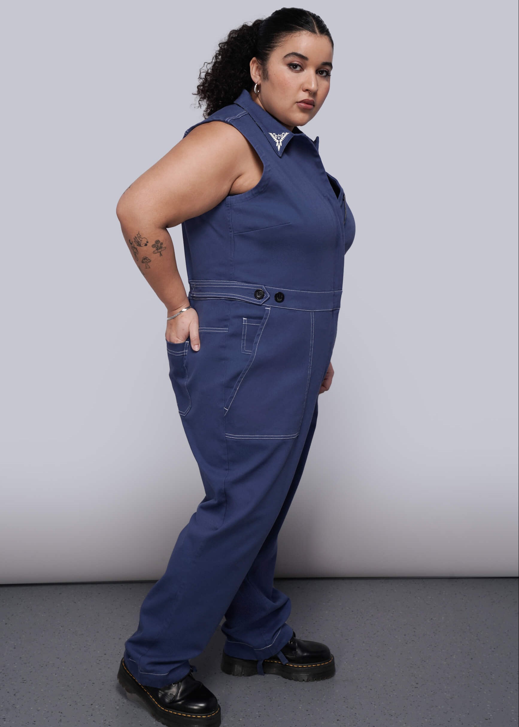 1X=Person wearing a blue sleeveless jumpsuit against a plain background