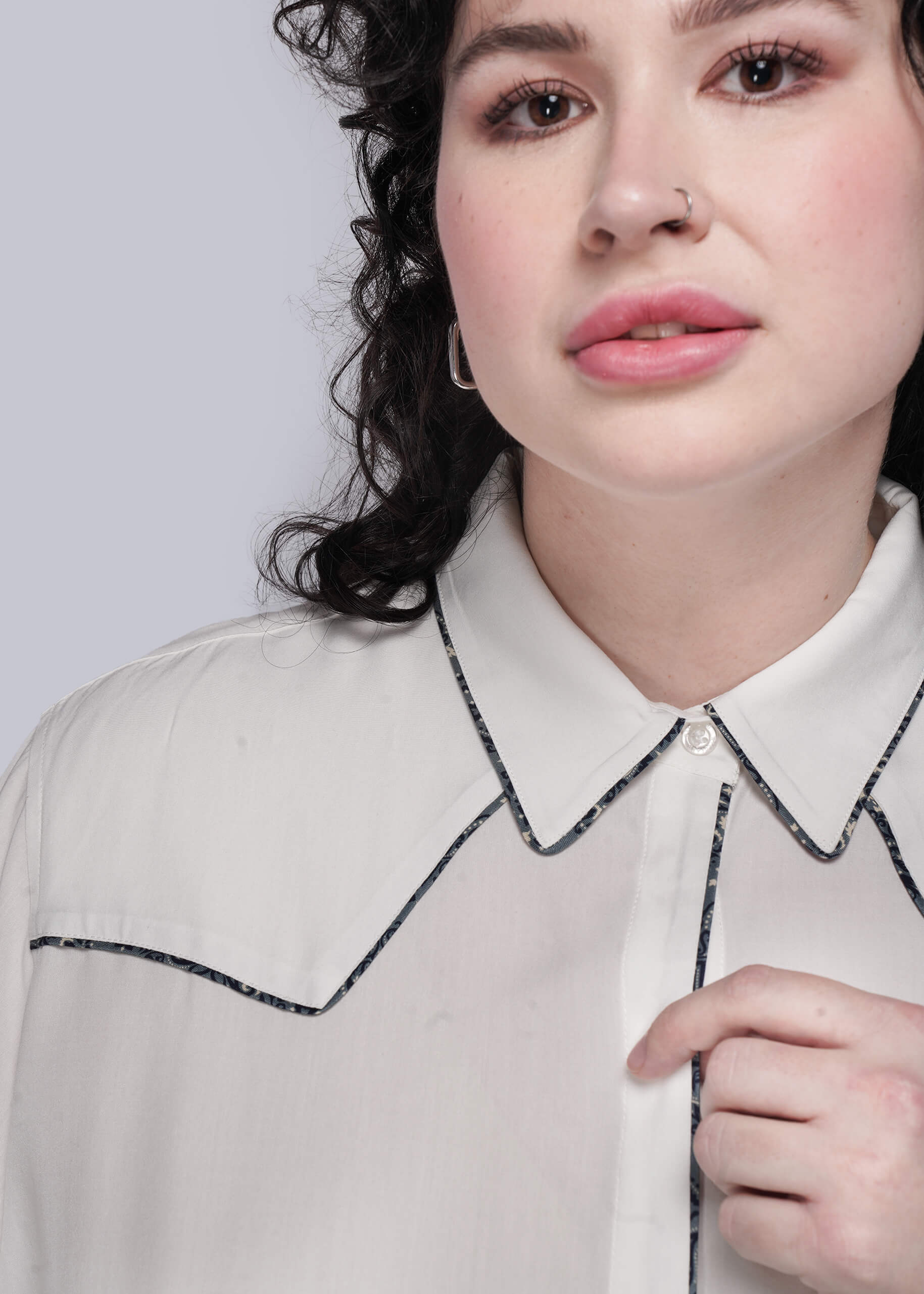 1X=Close-up of a person wearing a white shirt with decorative print trim on a light gray background