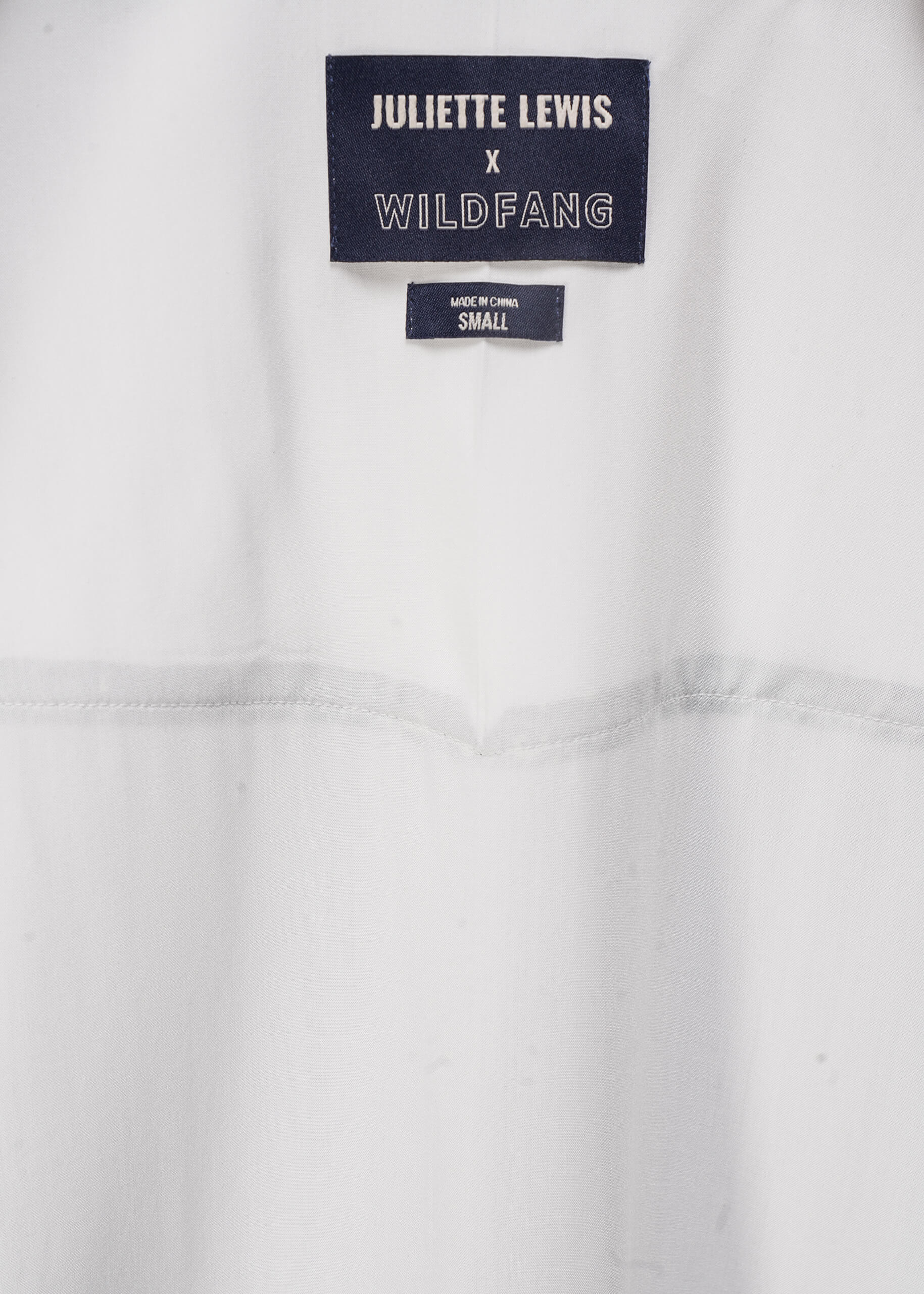 Close-up of interior of white button up shirt with 'Juliette Lewis x Wildfang' label 