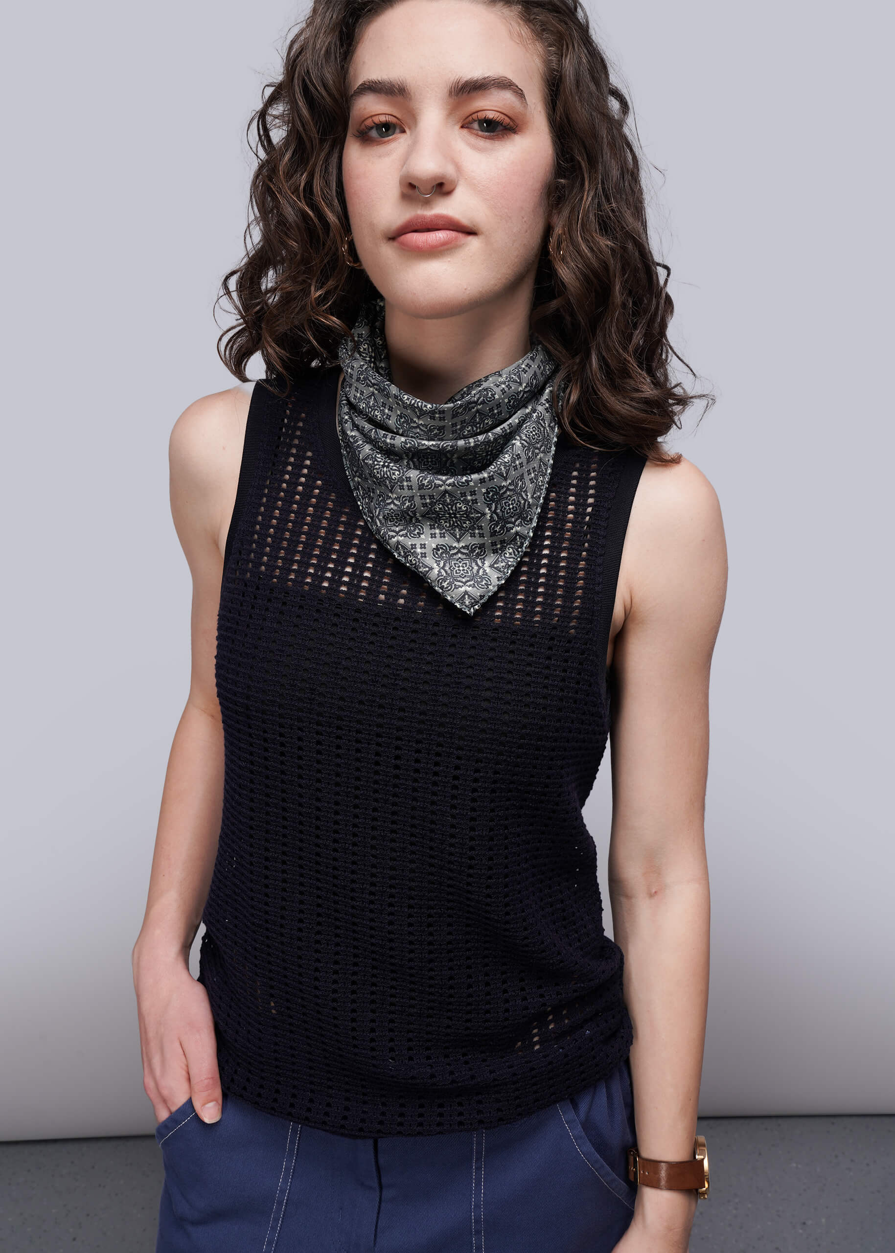 S=Woman wearing a black sleeveless knit mesh top with a patterned scarf against a plain background