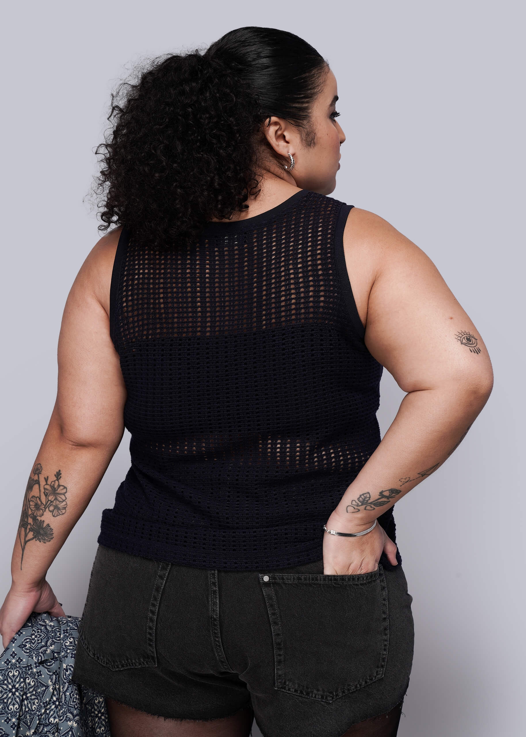 1X=Person wearing a navy blue knit mesh sleeveless top with black denim shorts on a plain background