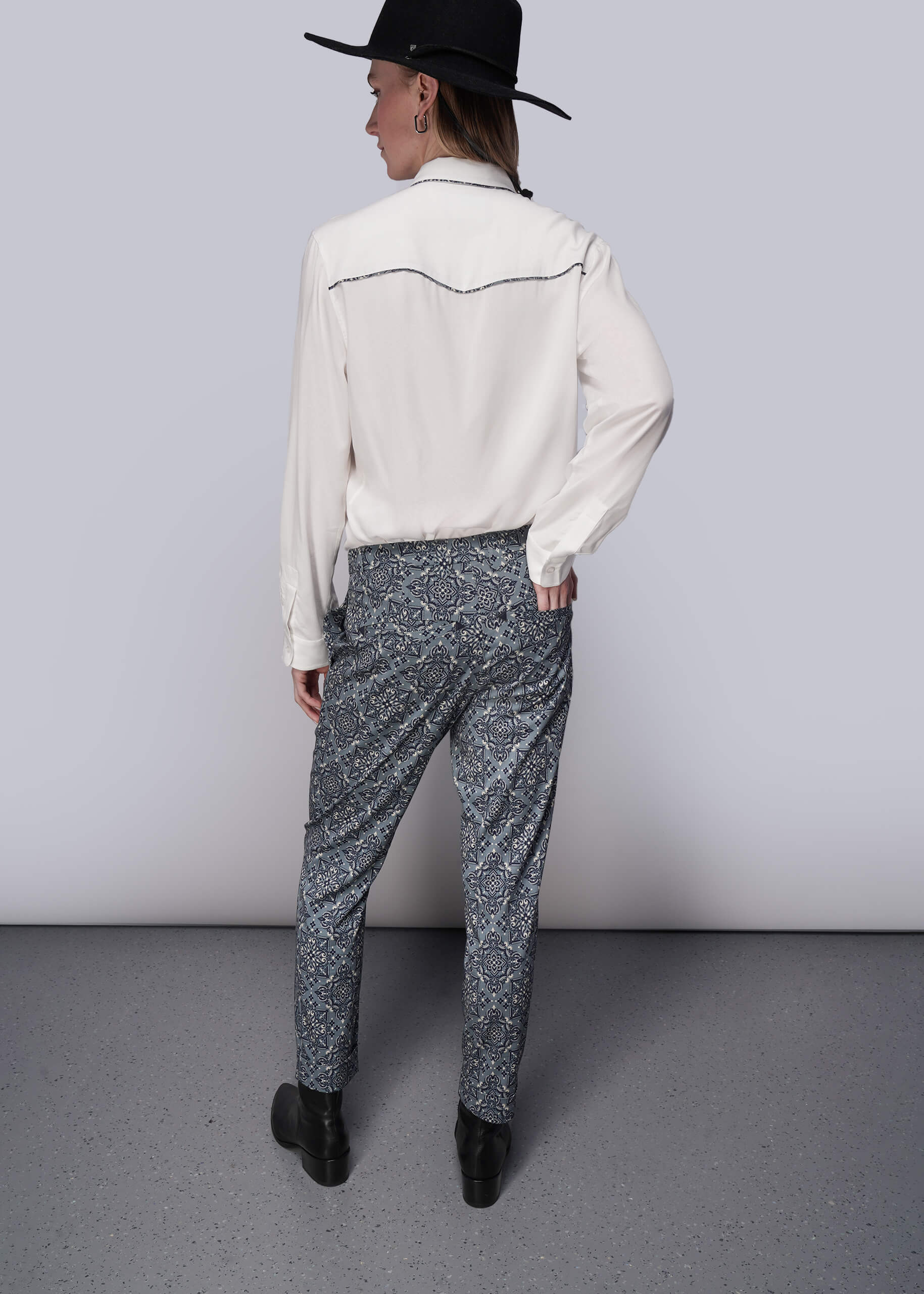 S=Person wearing a white shirt and patterned pants with a black hat on a plain background