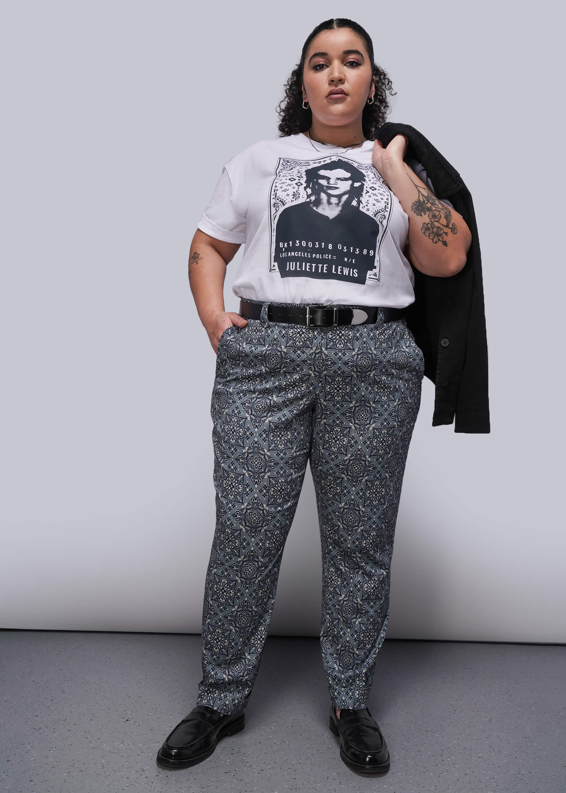1X=Person wearing a graphic t-shirt and patterned pants against a plain background