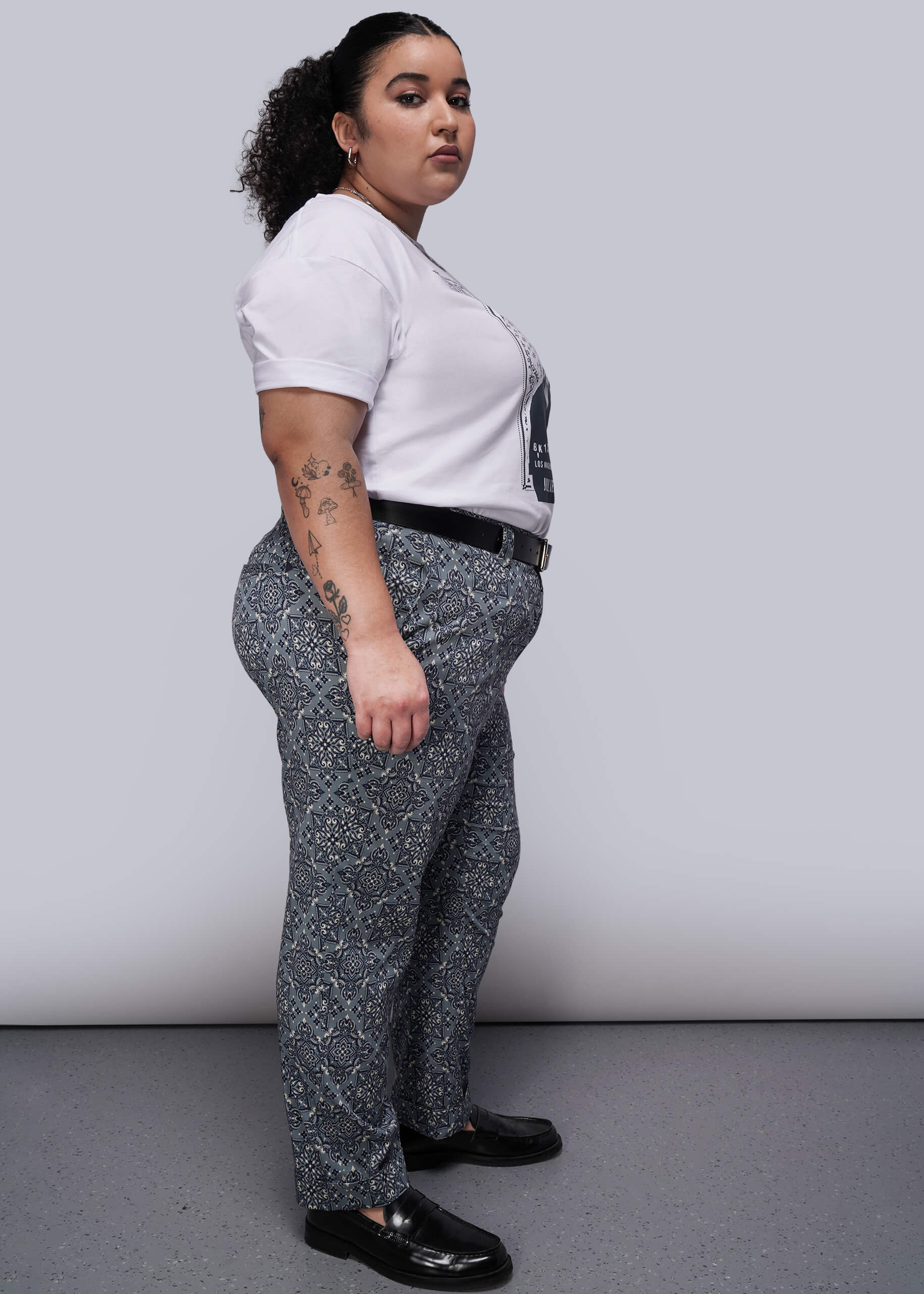 1X=Person wearing a white shirt and patterned pants against a plain background
