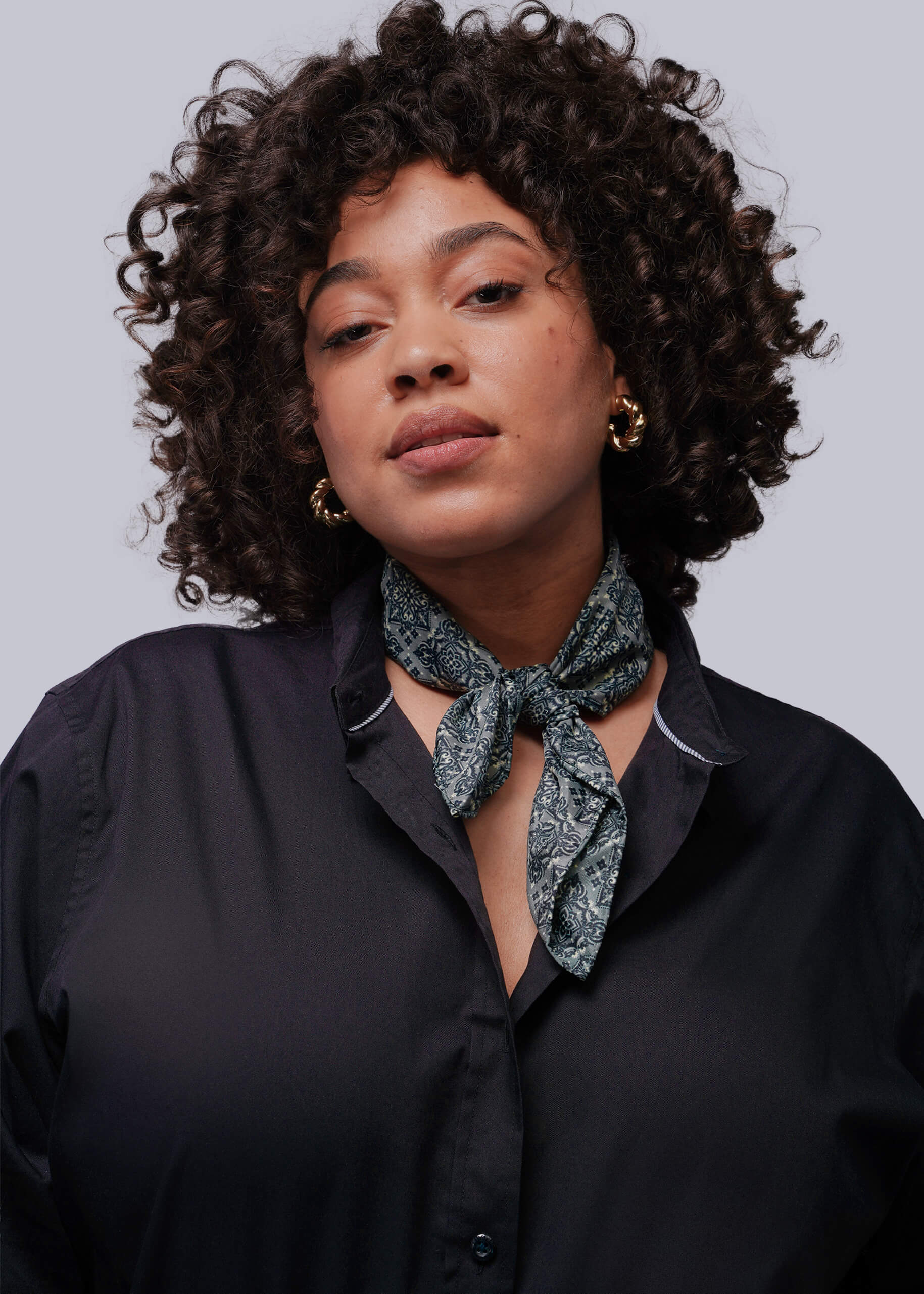 Woman wearing a black shirt with a patterned scarf around her neck against a gray background