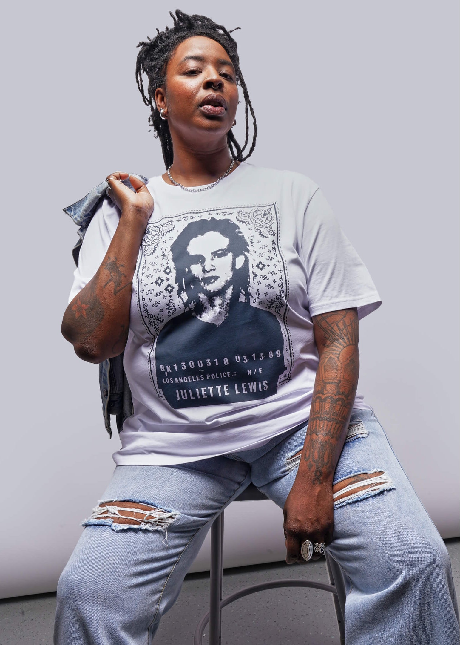 1X=Person wearing a t-shirt with a graphic design, sitting on a stool against a plain background