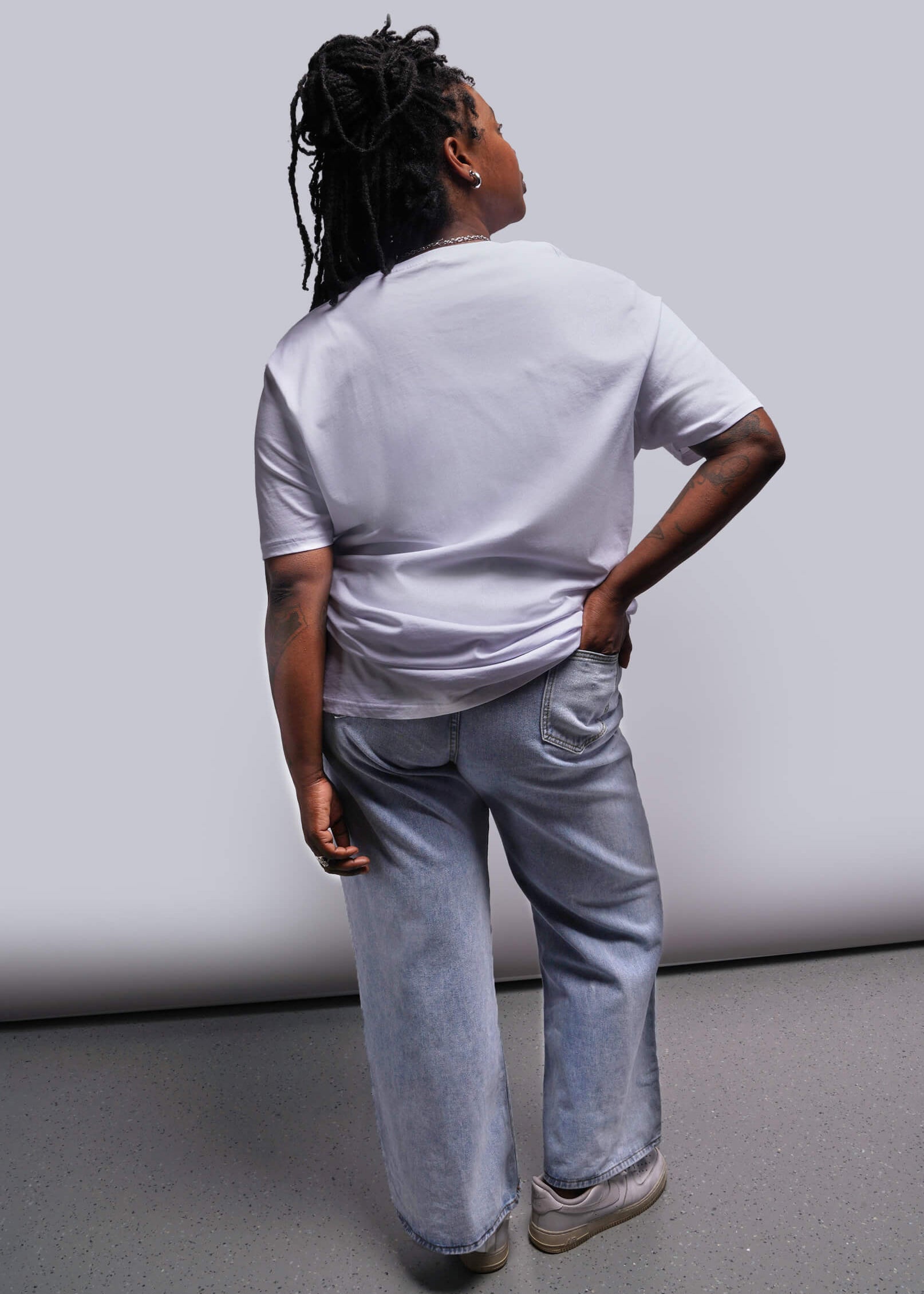 1X=Person wearing a white shirt and light blue jeans standing against a plain background