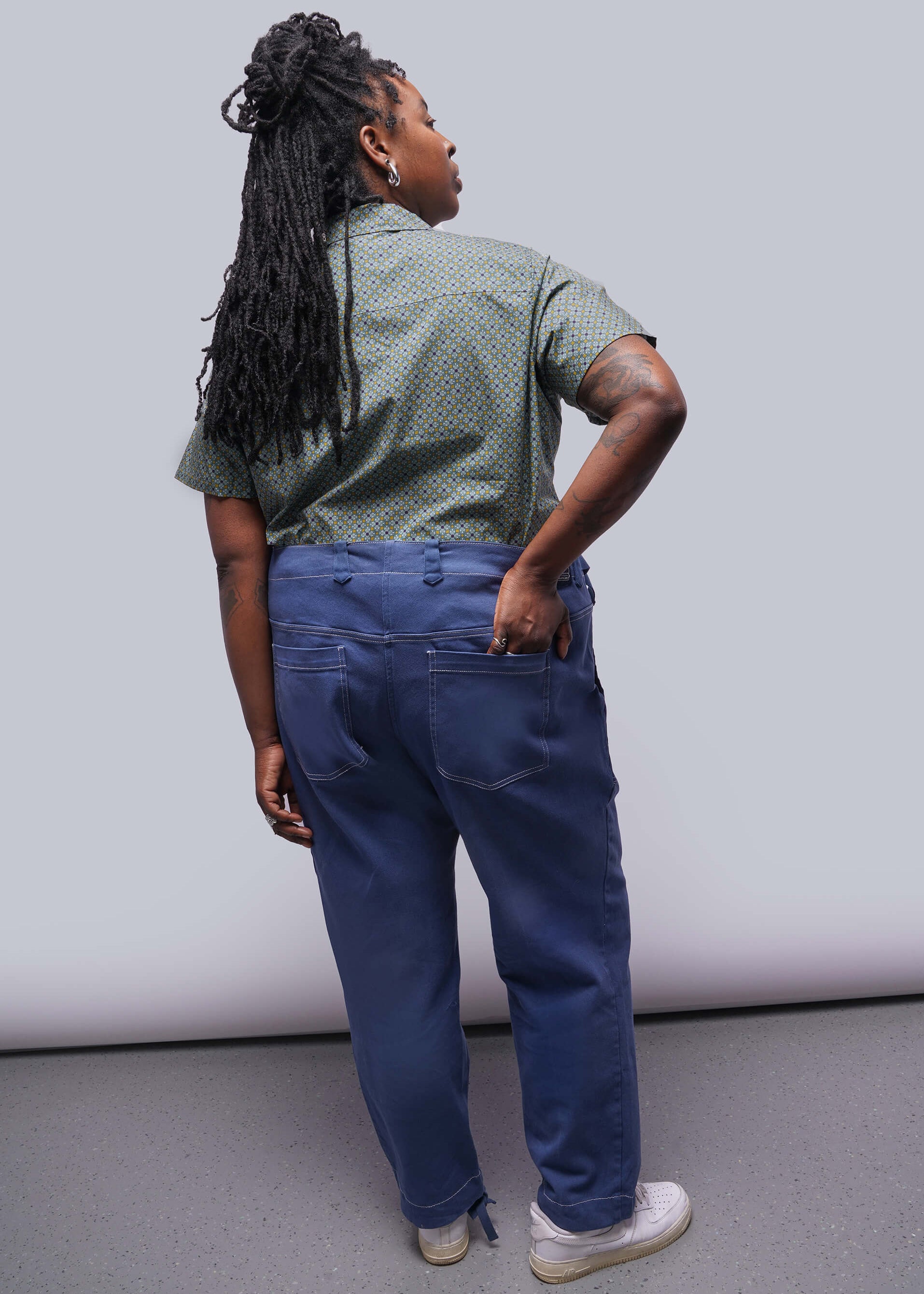 1X=Back of person wearing a green patterned shirt and blue pants against a plain background