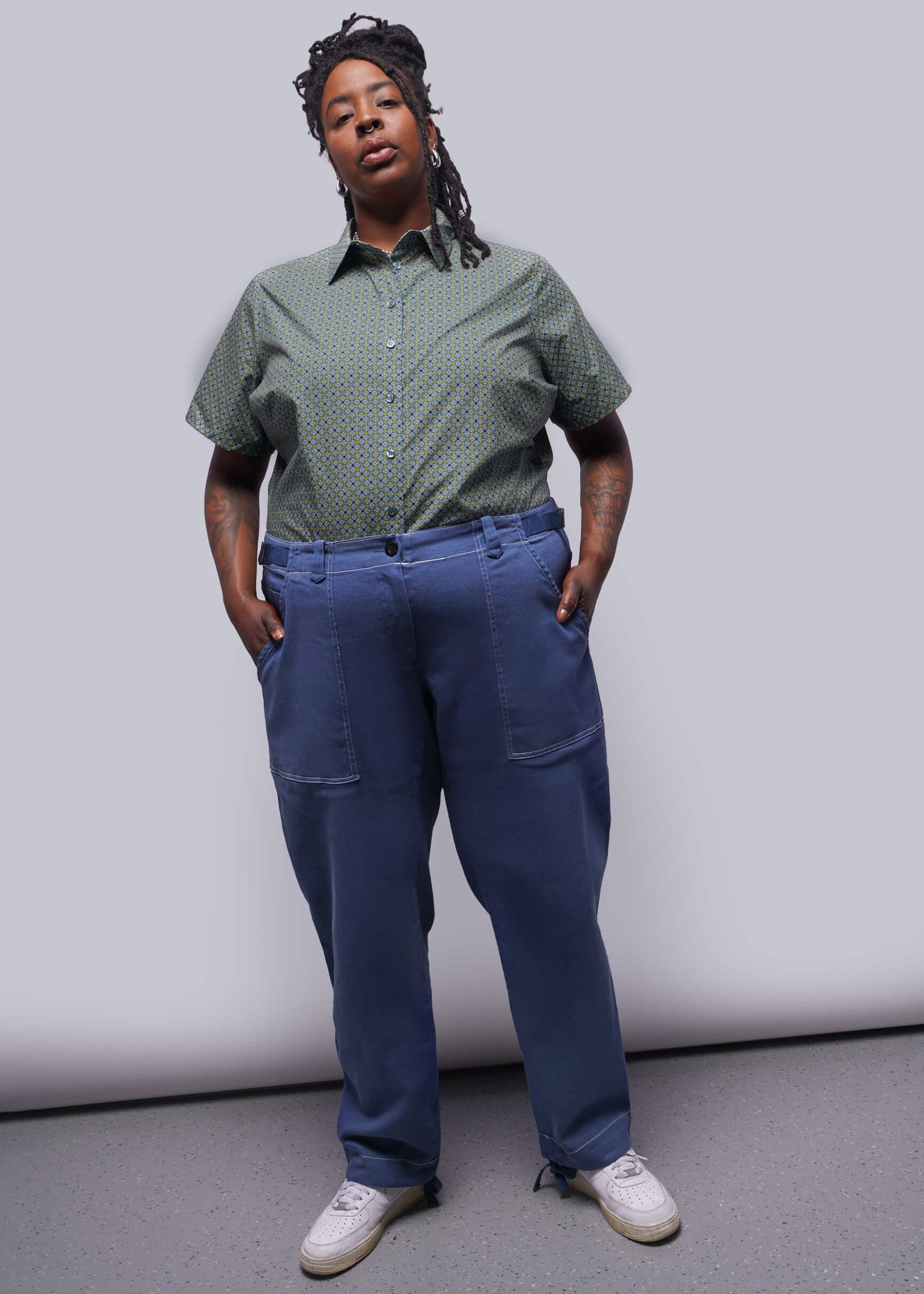 1X=Person wearing a green shirt and blue pants against a plain background