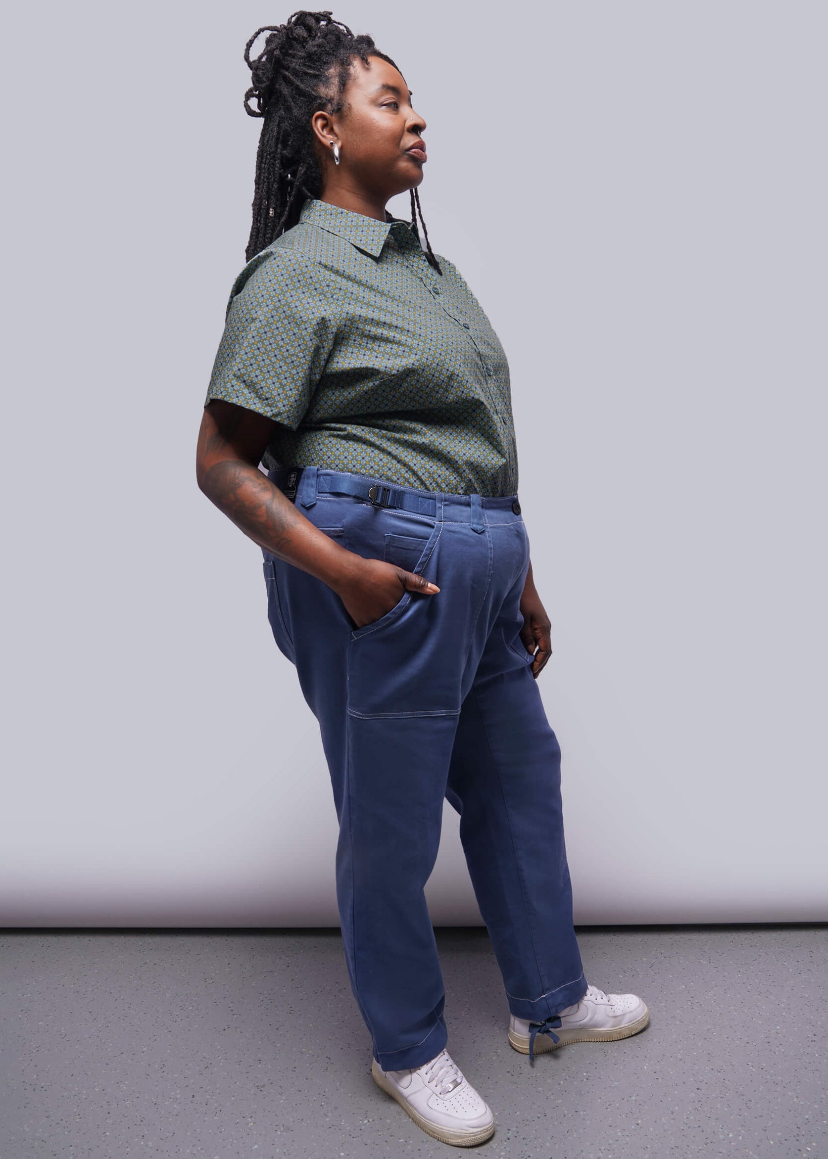 1X=Person wearing a green patterned shirt and blue pants against a plain background