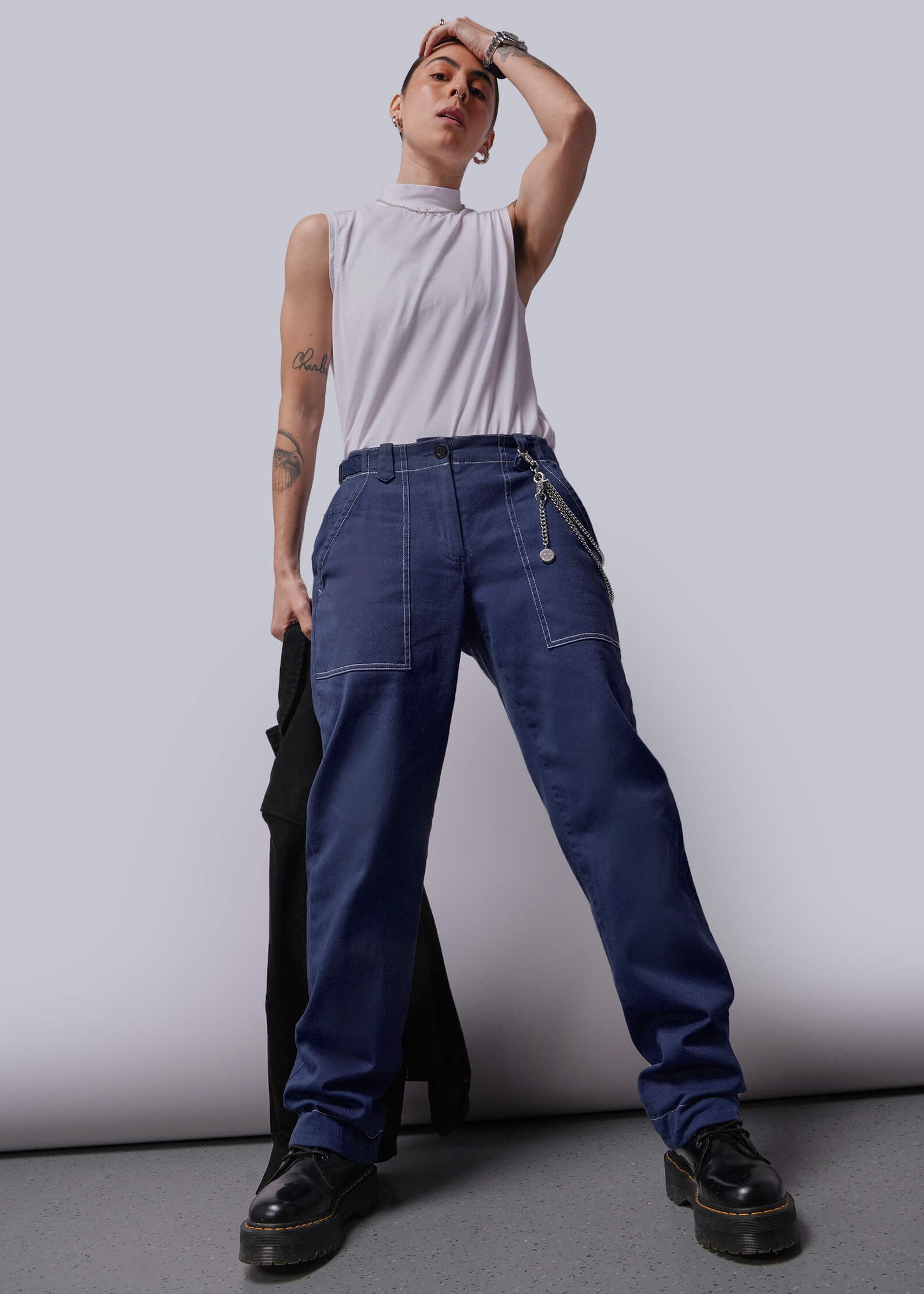 Person wearing a white sleeveless top and blue denim pants against a plain background