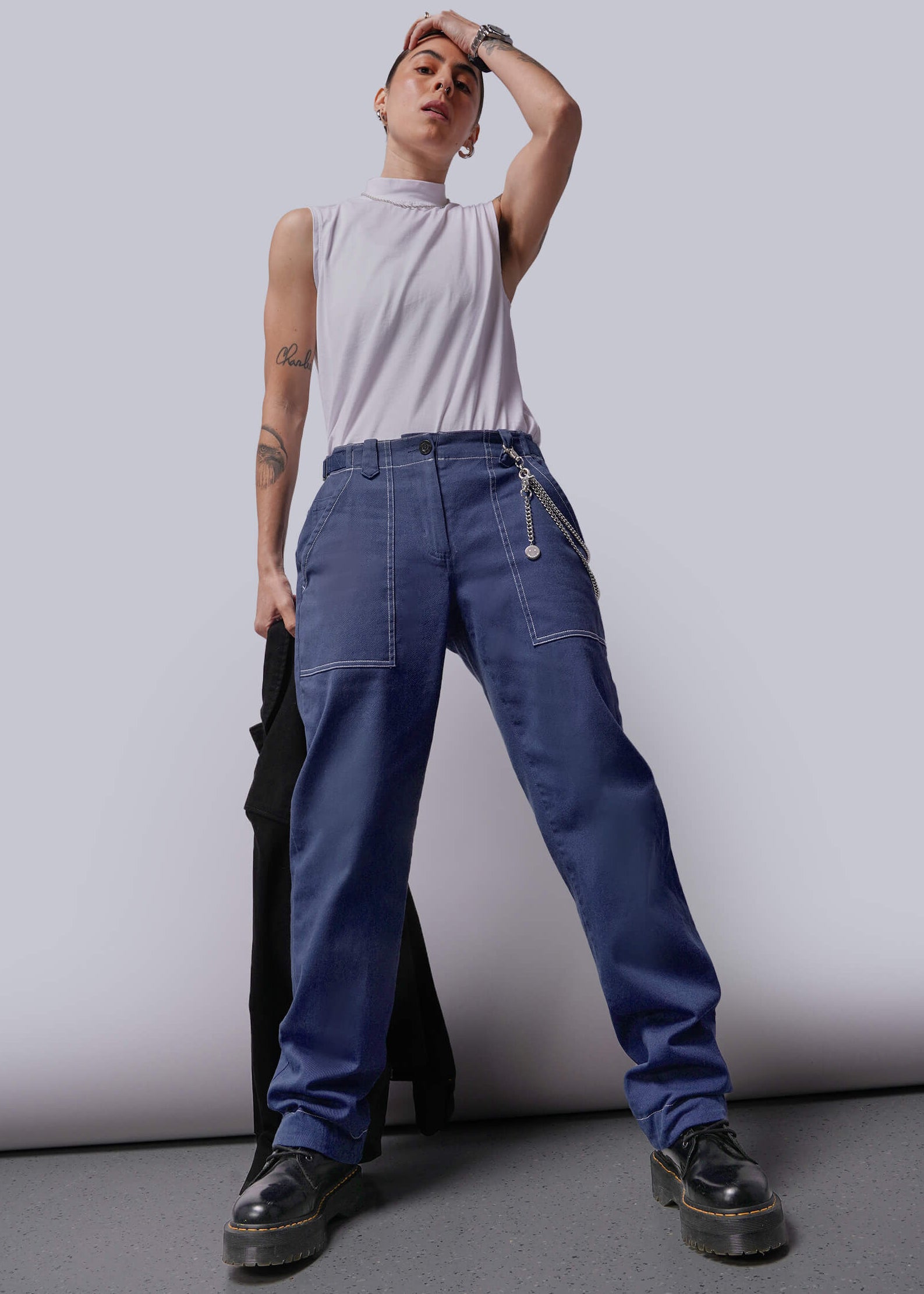 S=Person wearing a white sleeveless top and blue denim pants against a plain background