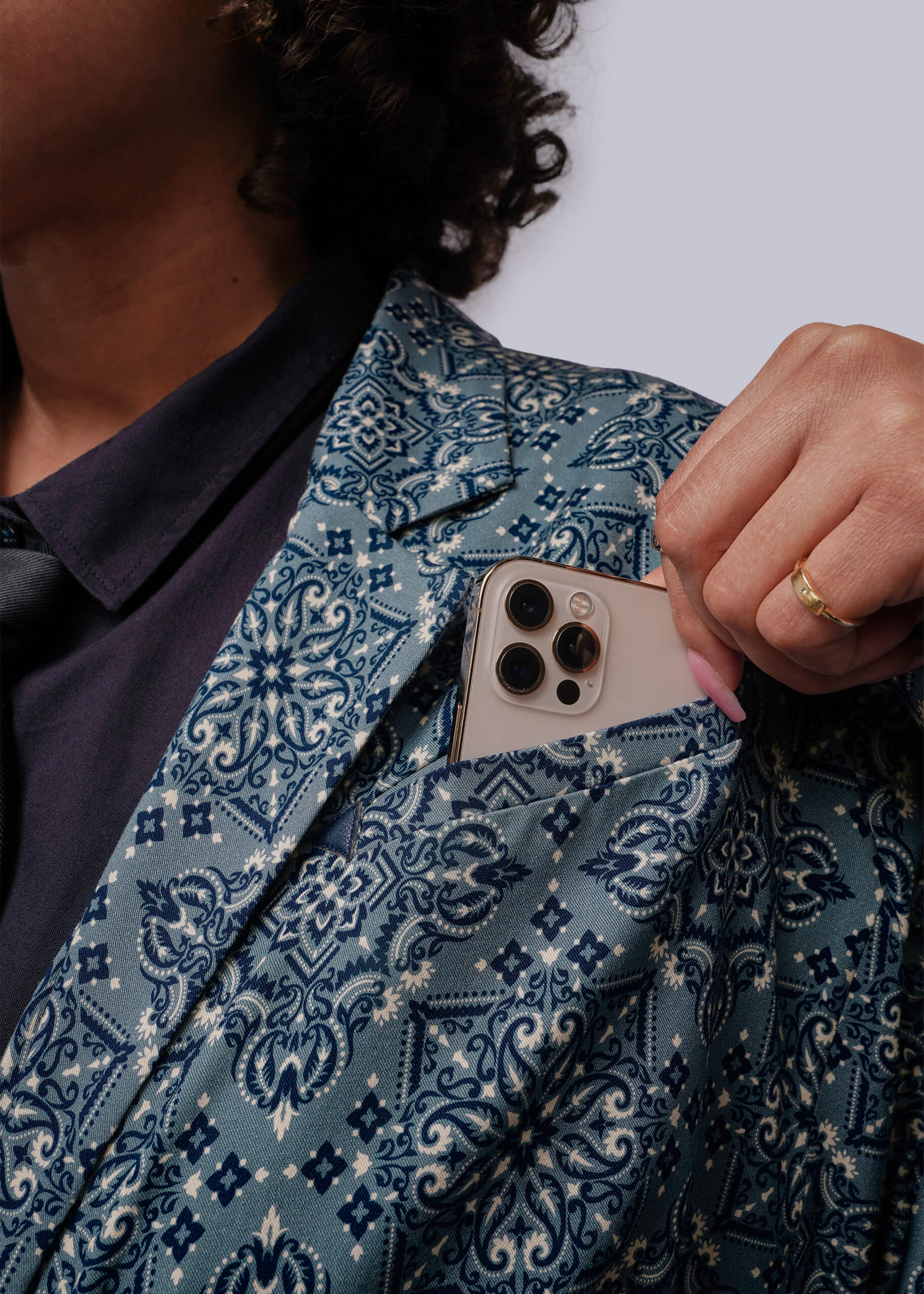 1X=Person wearing a patterned blazer placing a phone in the chest pocket against a white background