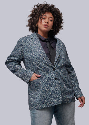 1X=Person wearing a patterned blazer and jeans on a plain background