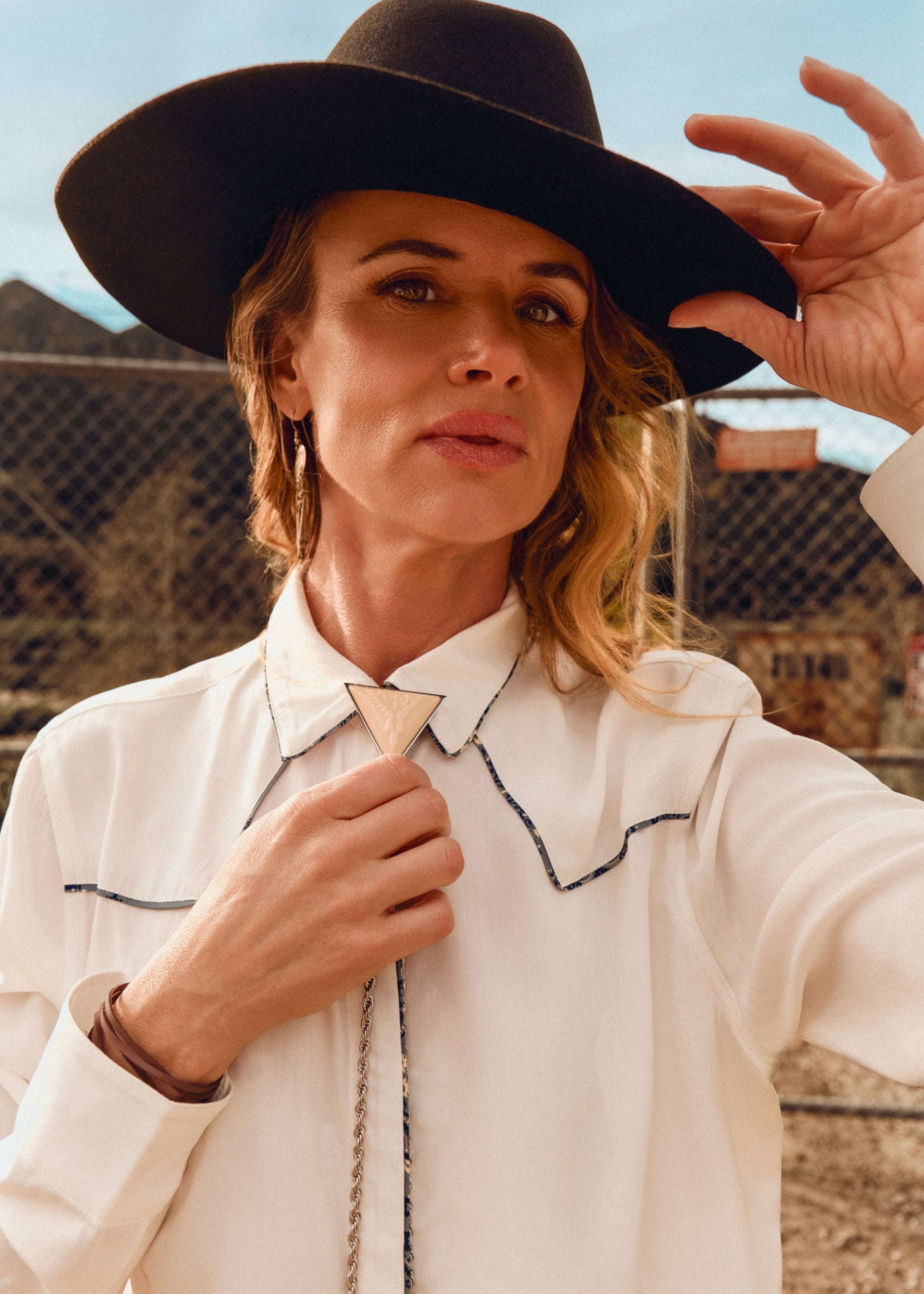 Person wearing a wide-brimmed hat and white shirt with a bolo tie, outdoors.