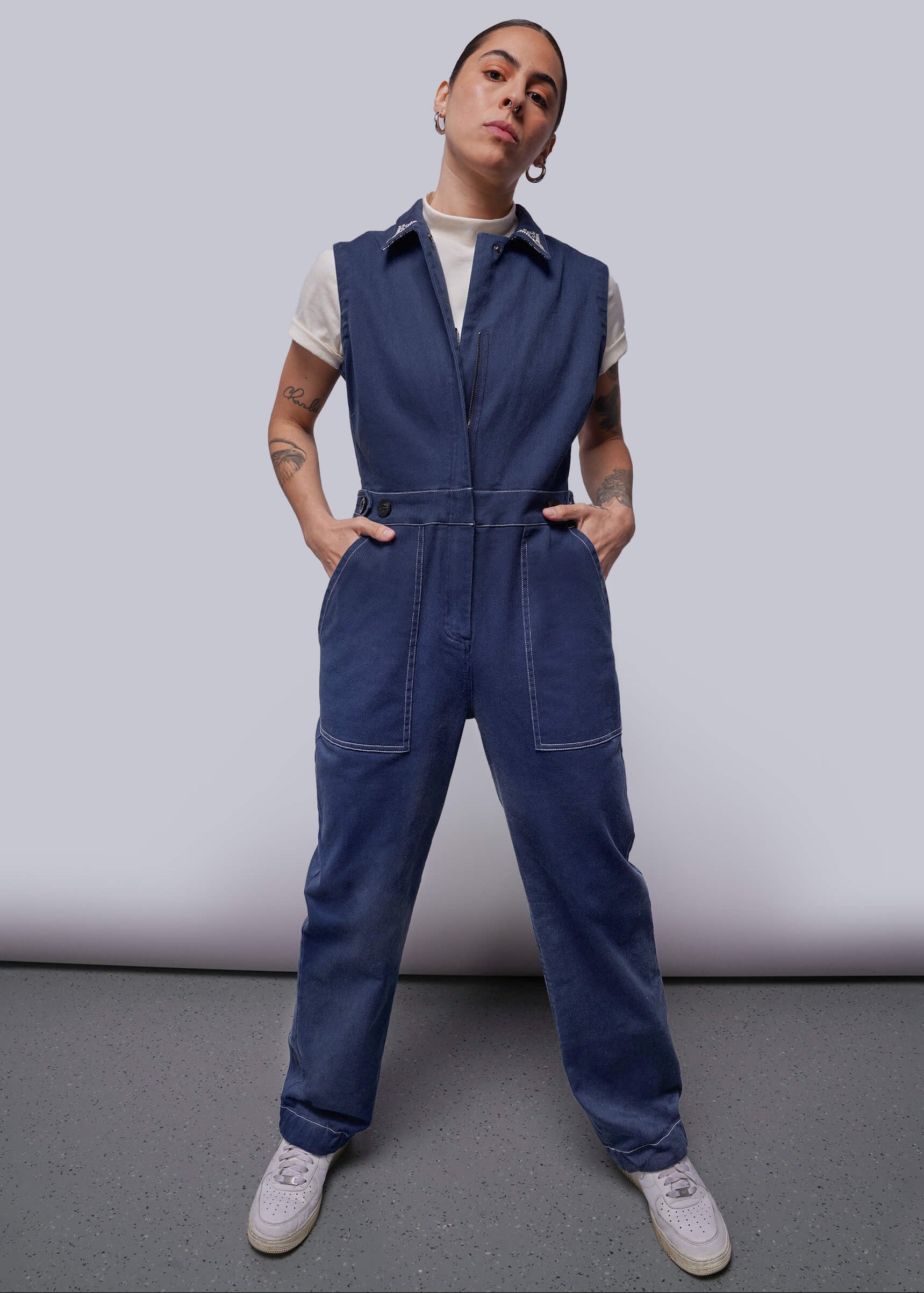 Person wearing a blue denim jumpsuit with white shirt underneath against a plain background