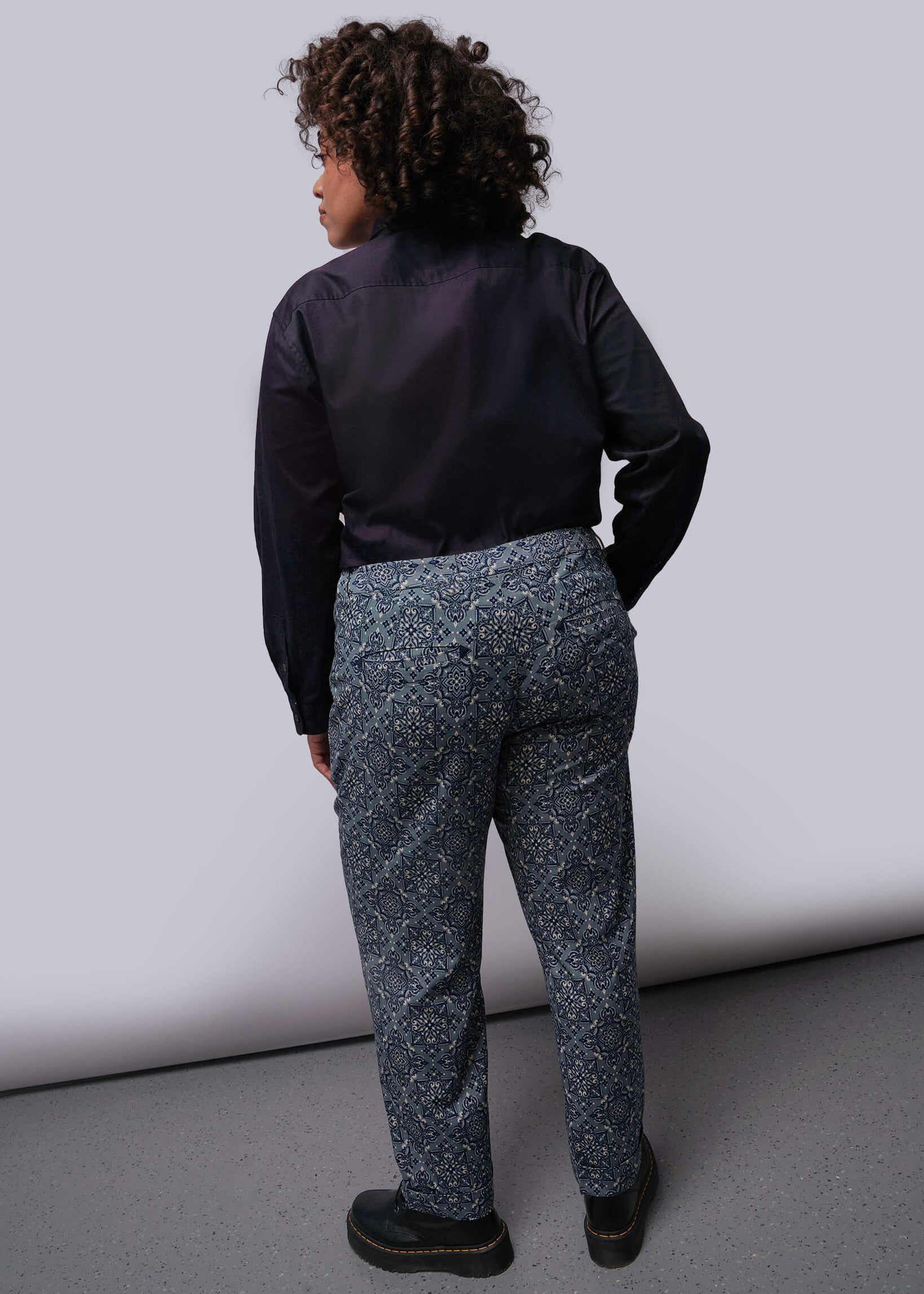 1X-Back of person wearing a black button up shirt and patterned pants against a plain background
