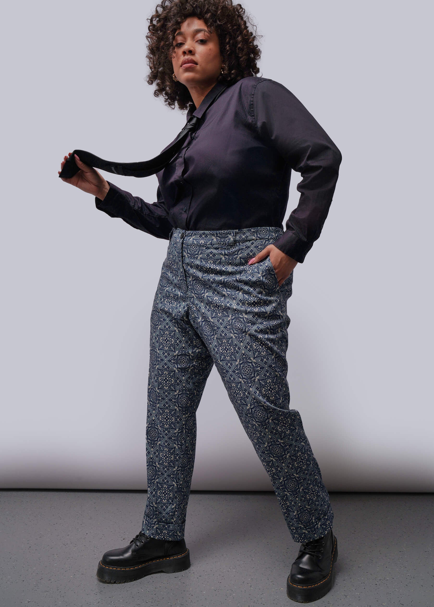 1X=Person wearing a black shirt and patterned pants against a plain background