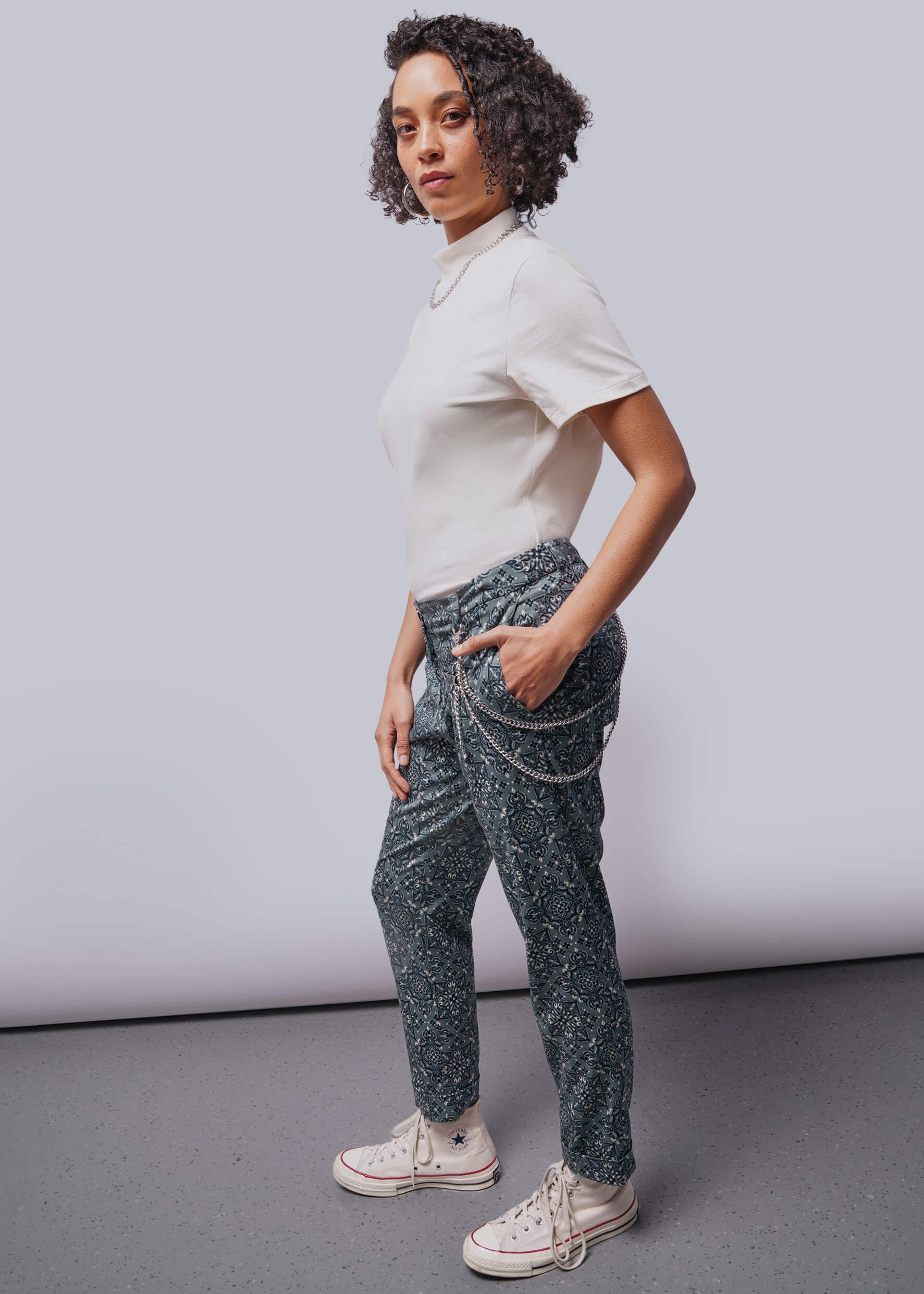 S=Person wearing a white shirt and patterned pants against a plain background