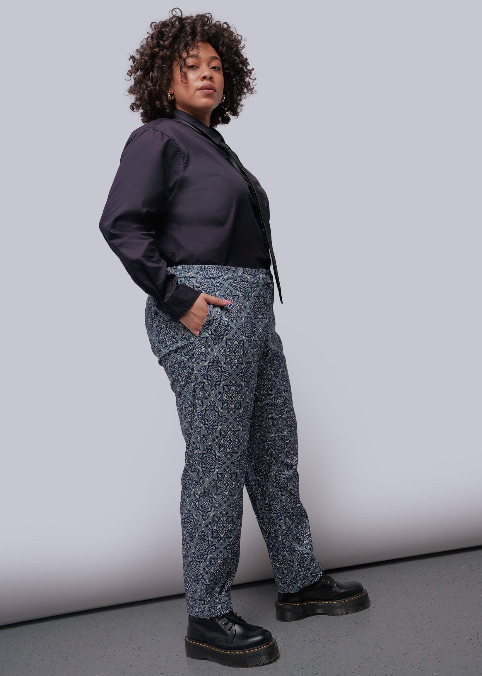 1X=Person wearing a black shirt and patterned pants against a plain background