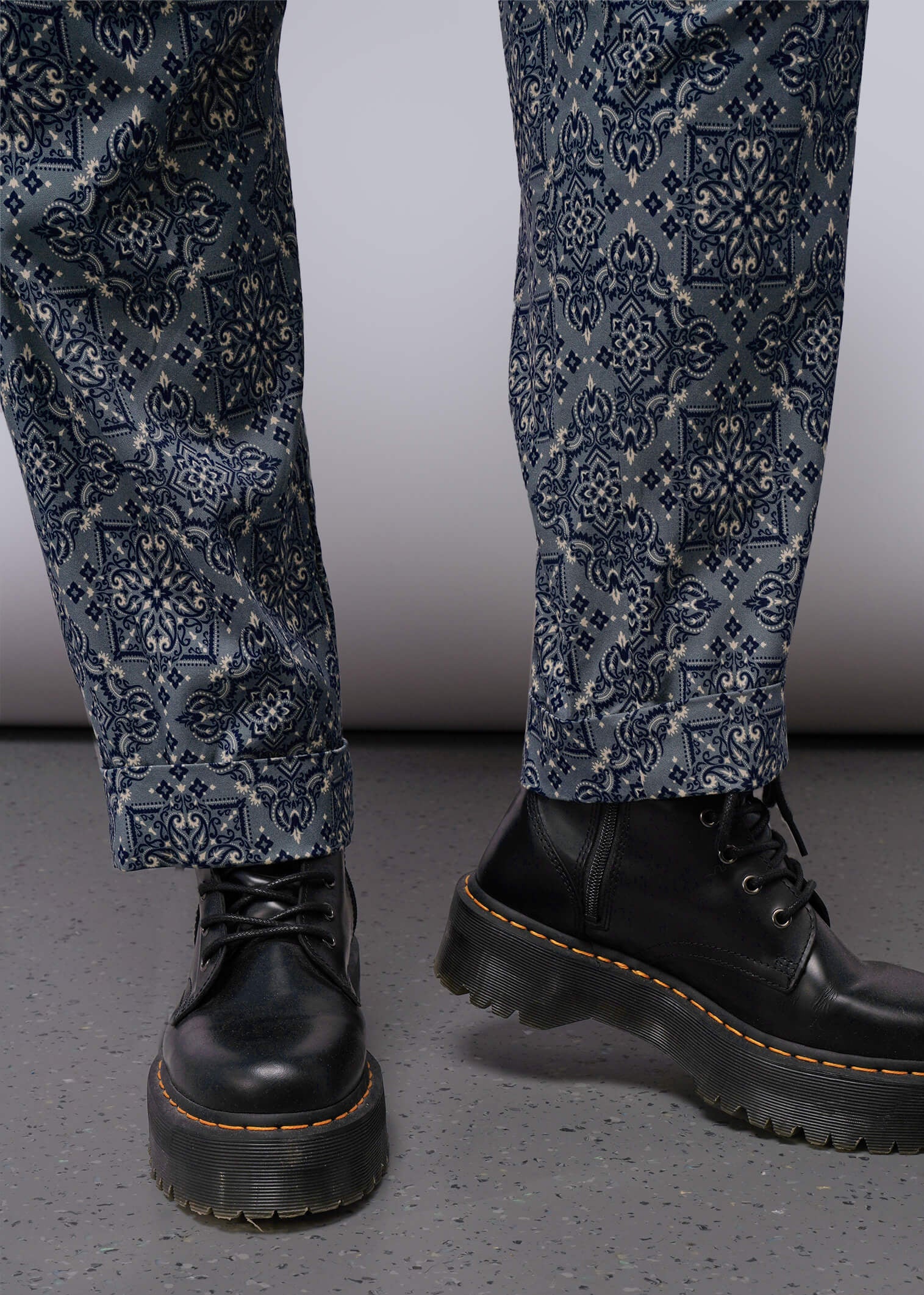 1X=Black leather boots and patterned pants on a neutral background