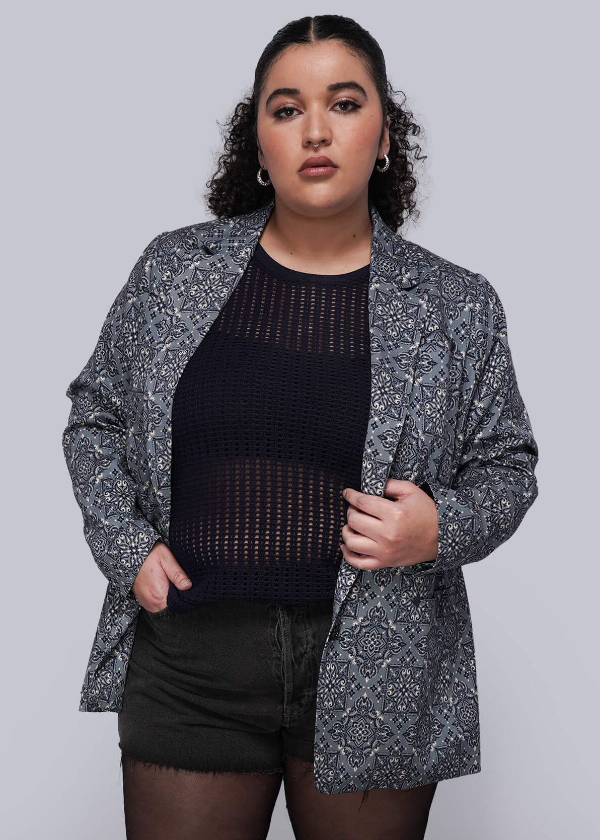 1X=Person wearing a patterned blazer, navy blue mesh top, and shorts against a plain background