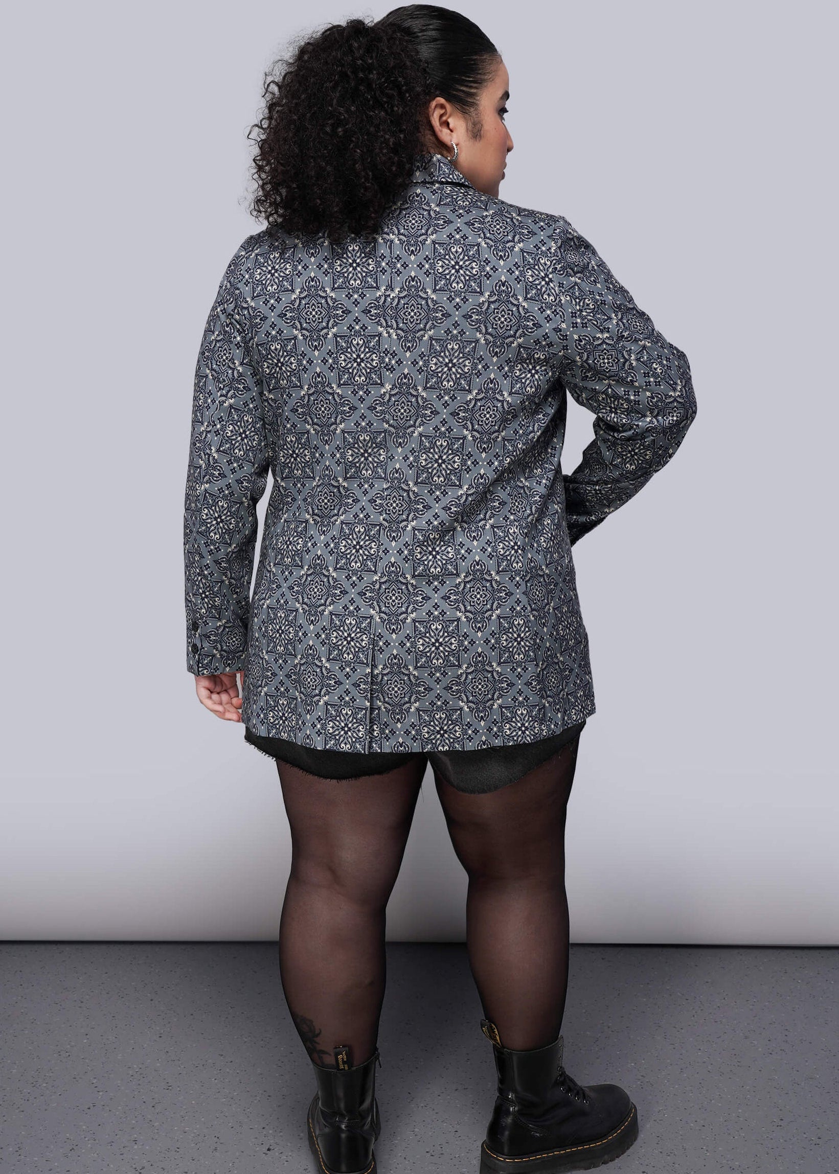 1X=Person wearing a patterned blazer against a plain background