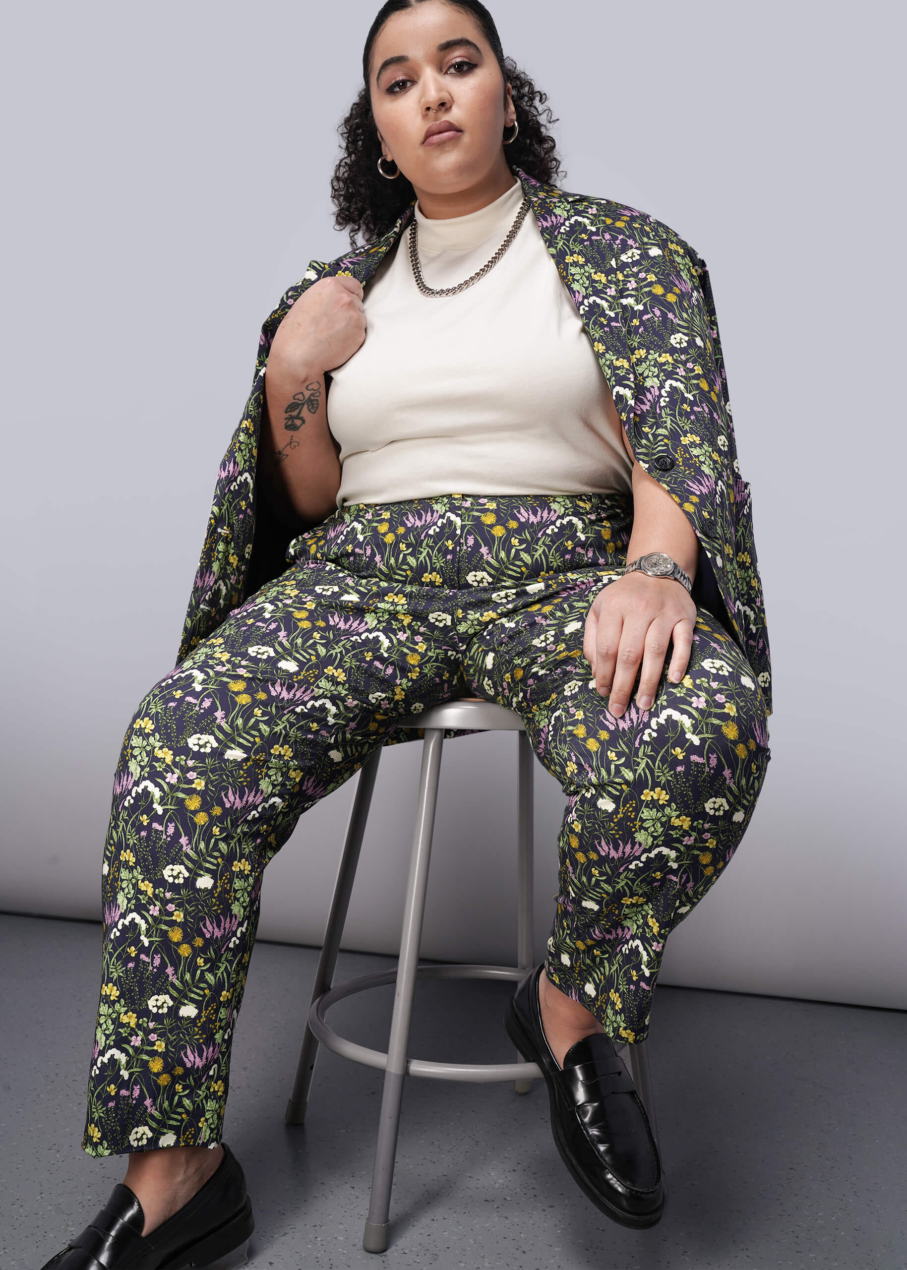 1X=Person wearing a floral suit sitting on a stool against a plain background