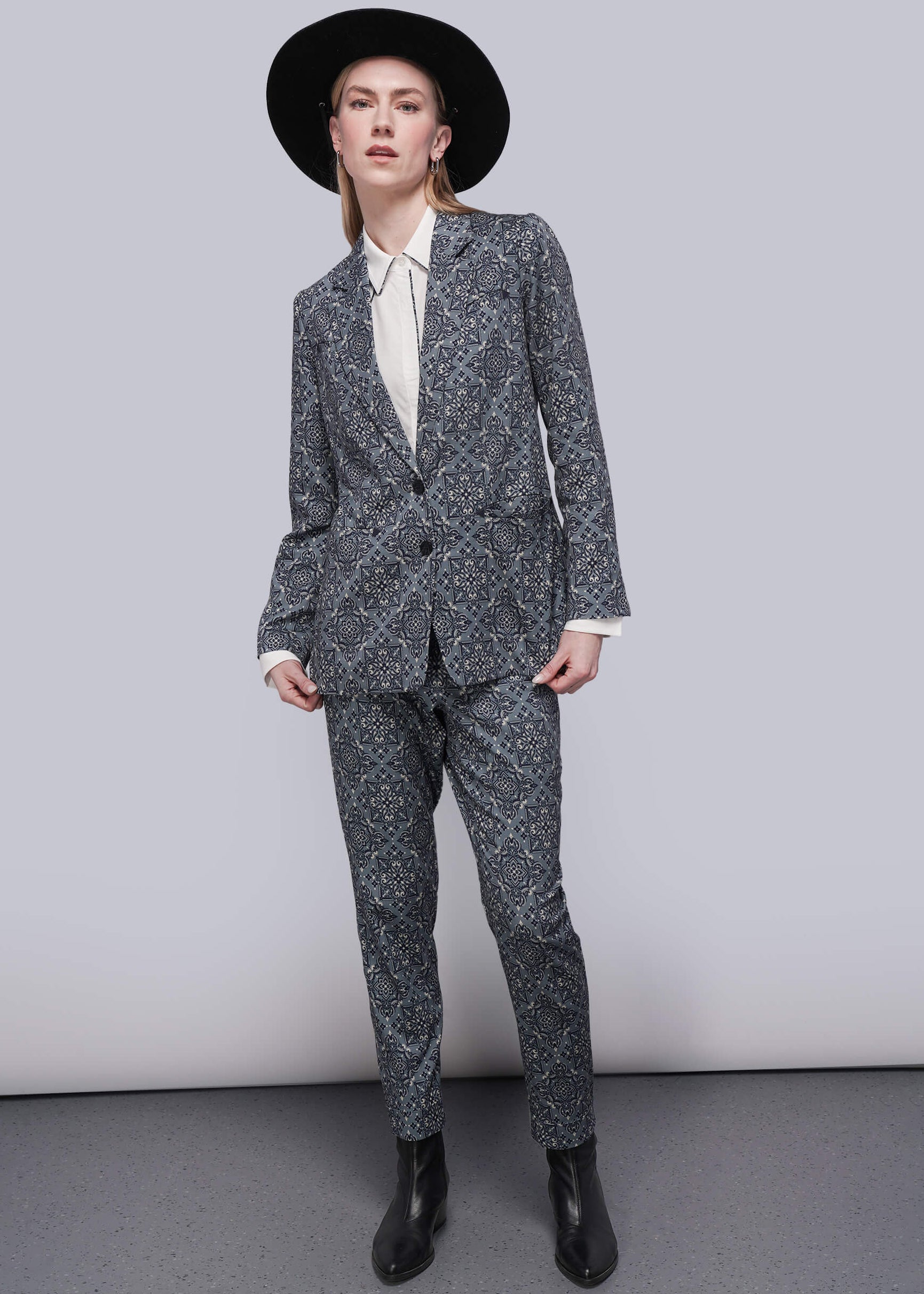 S=Person wearing a teal patterned suit and black hat against a plain background