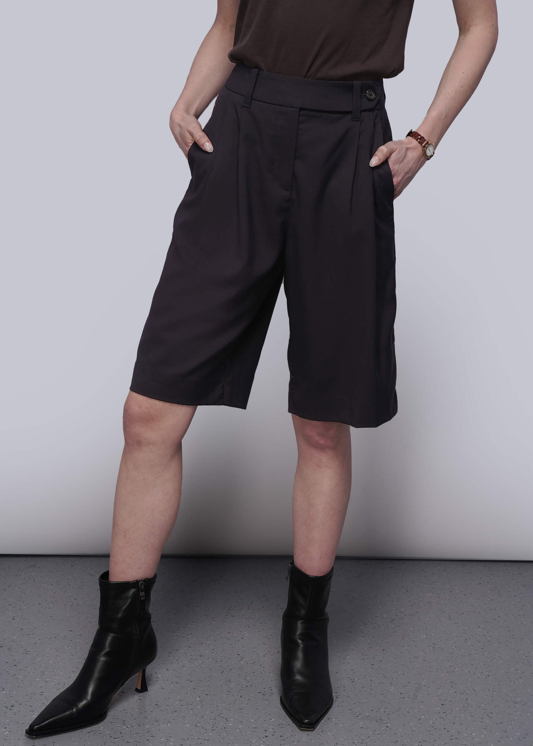 Person wearing black shorts and black boots against a plain background