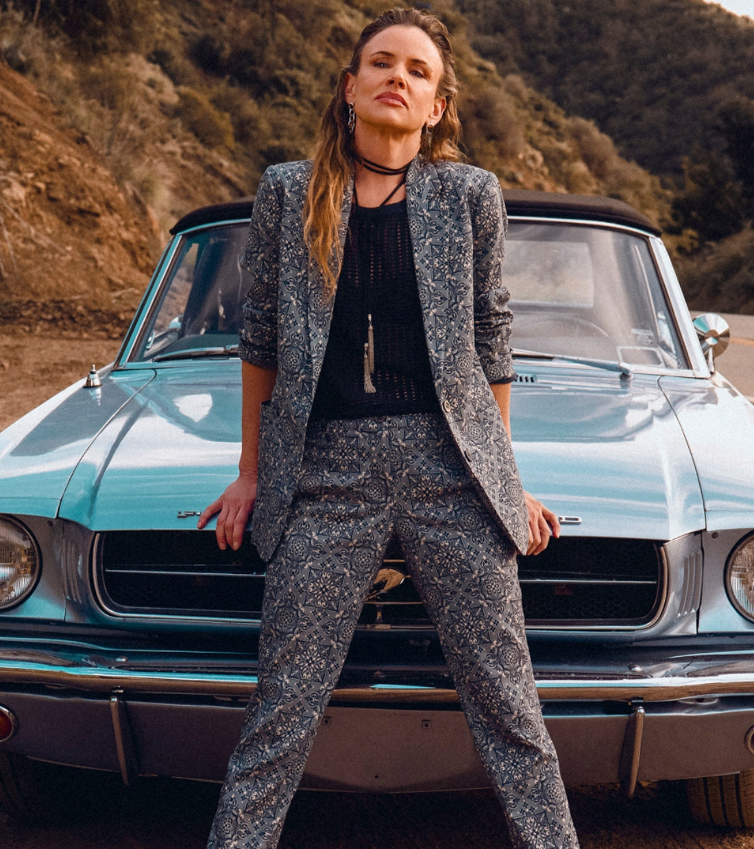 Juliette Lewis wearing teal bandana print suiting, stands in front of vintage blue car 