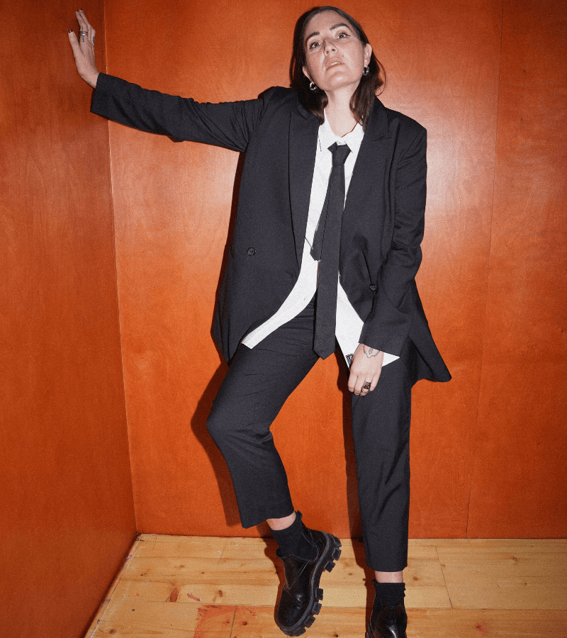 Person wearing a black suit and tie against an orange wall