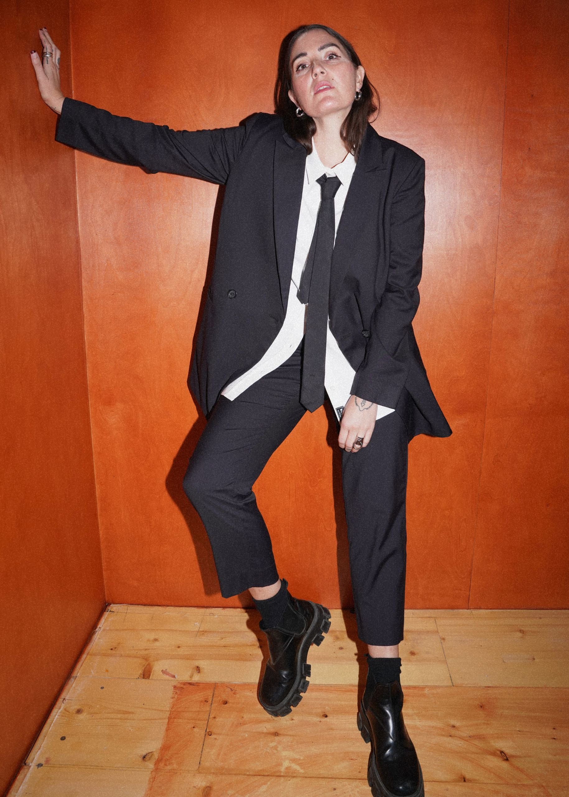 Person wearing a black suit with a white shirt and tie against an orange wall.