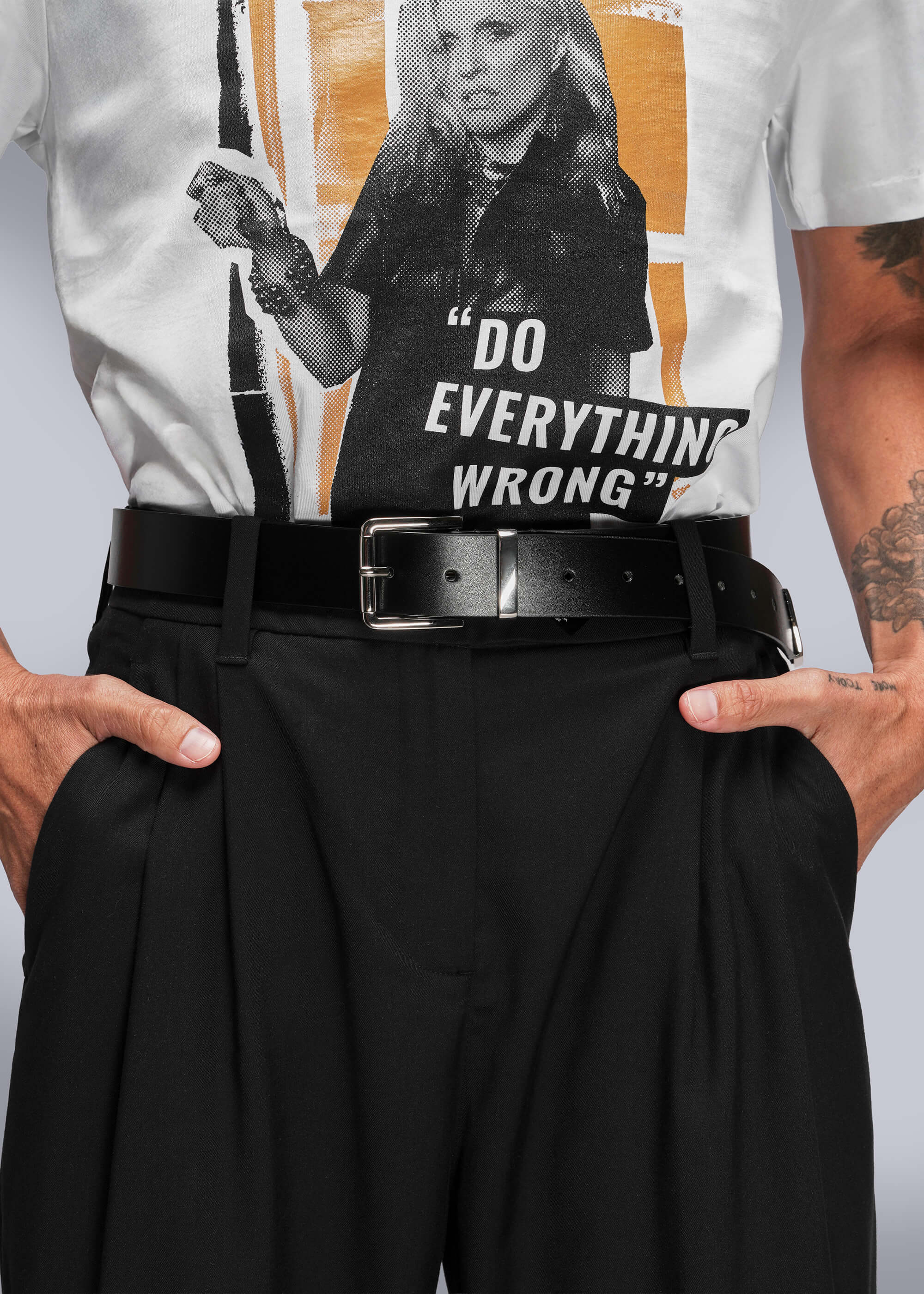 Person wearing a t-shirt with a graphic design and text, paired with black pants and a belt.
