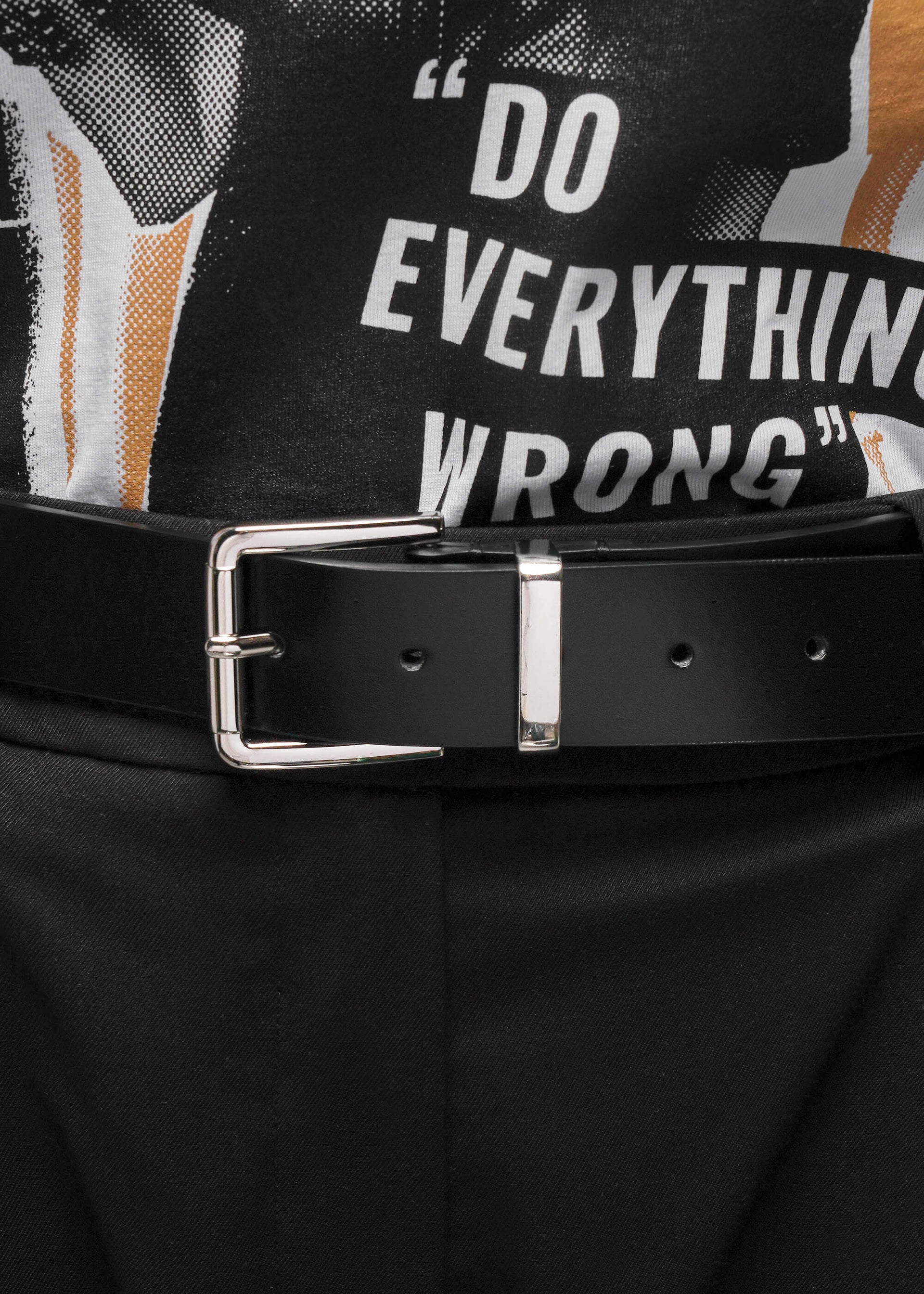 Black belt with silver buckle worn by a person wearing graphic tee and black pants.