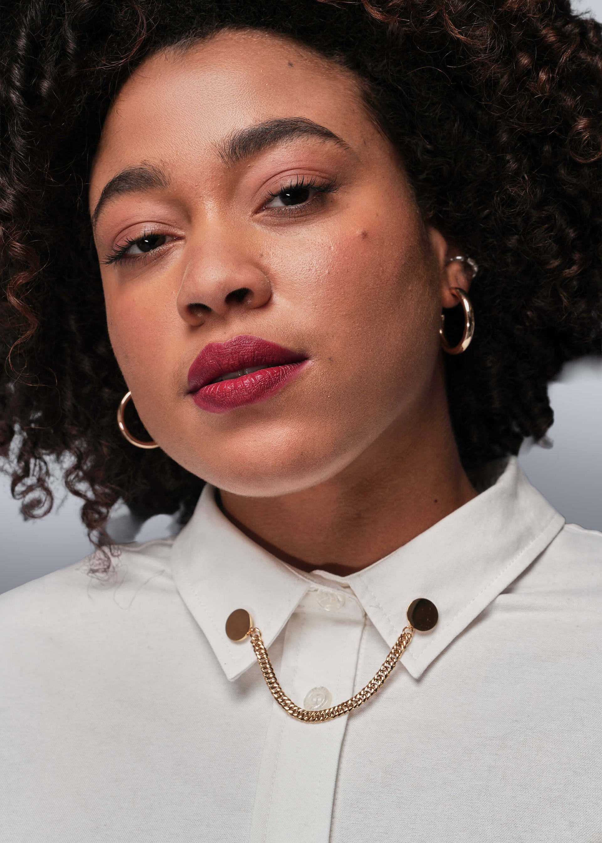 Person wearing a white shirt with a gold chain collar clips against a neutral background