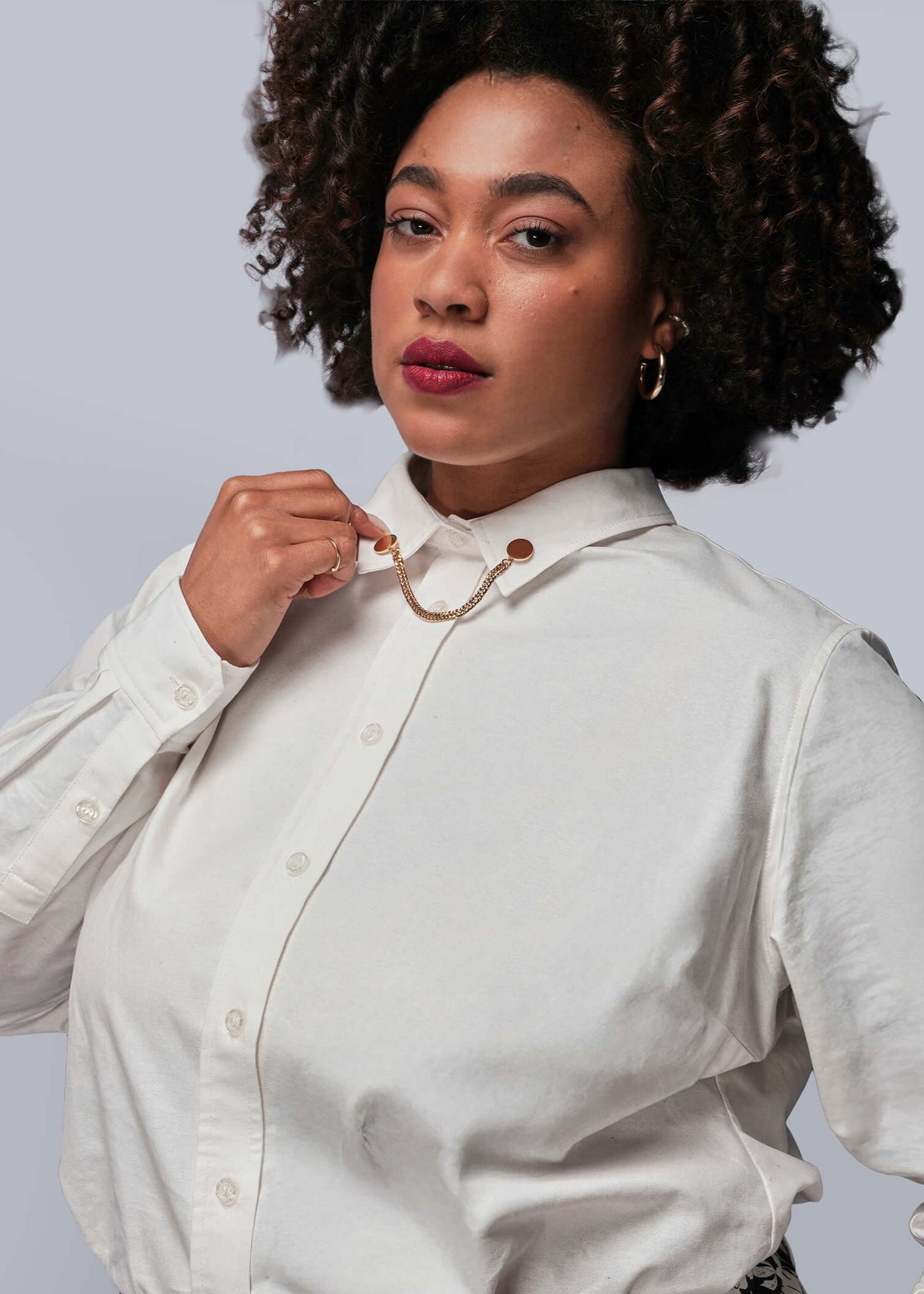 Woman adjusting the collar of a white blouse with gold collar clips against a plain background